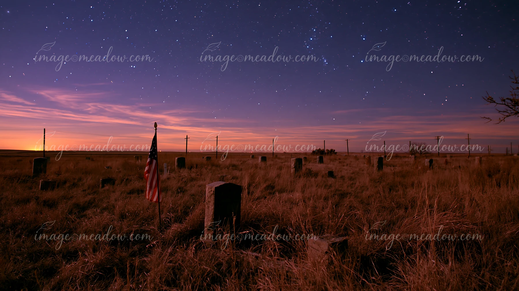 An American flag stands among graves at twilight under a starry sky.