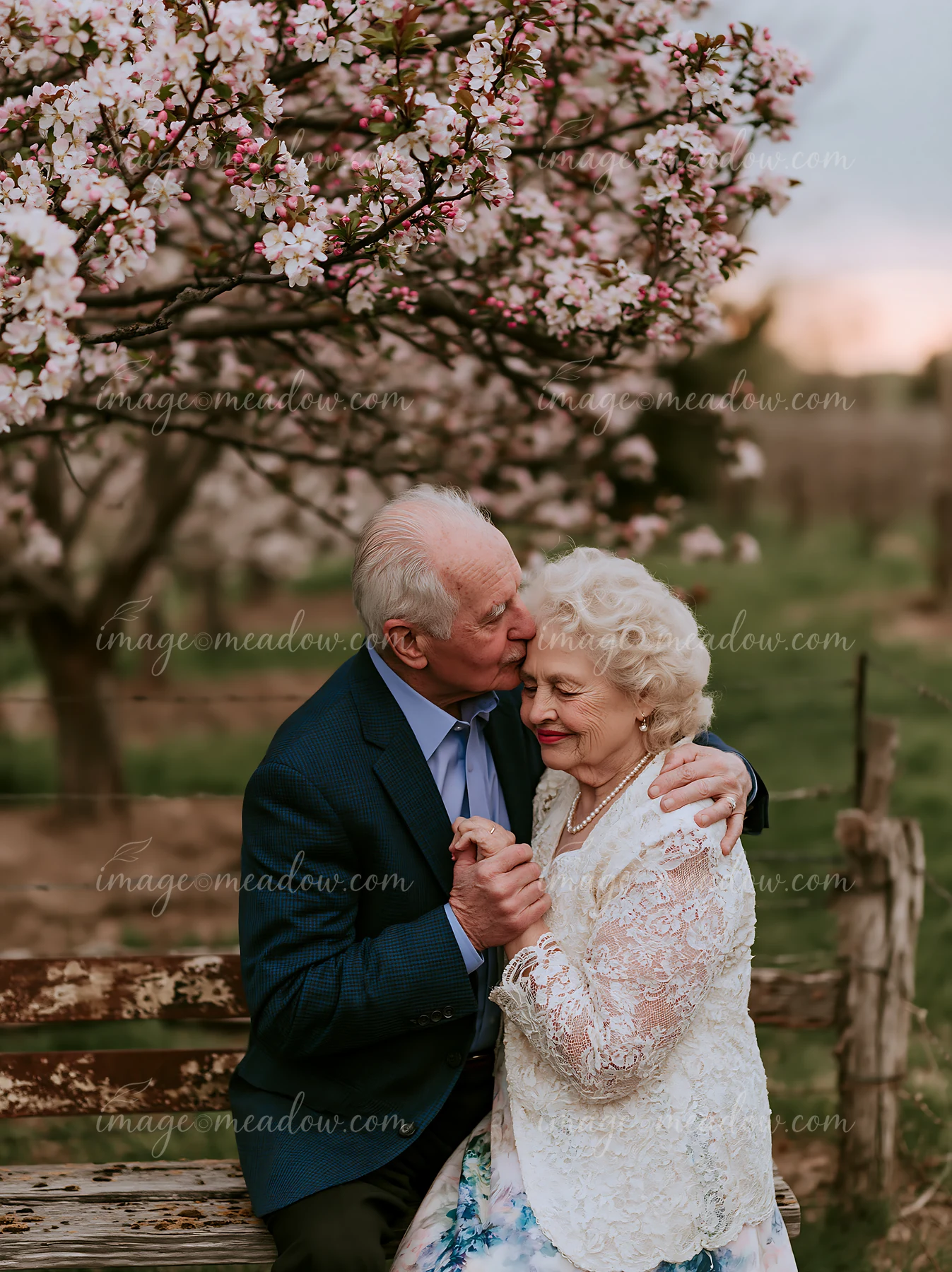 An elderly couple enjoys a gentle kiss among blooming flowers in a garden.