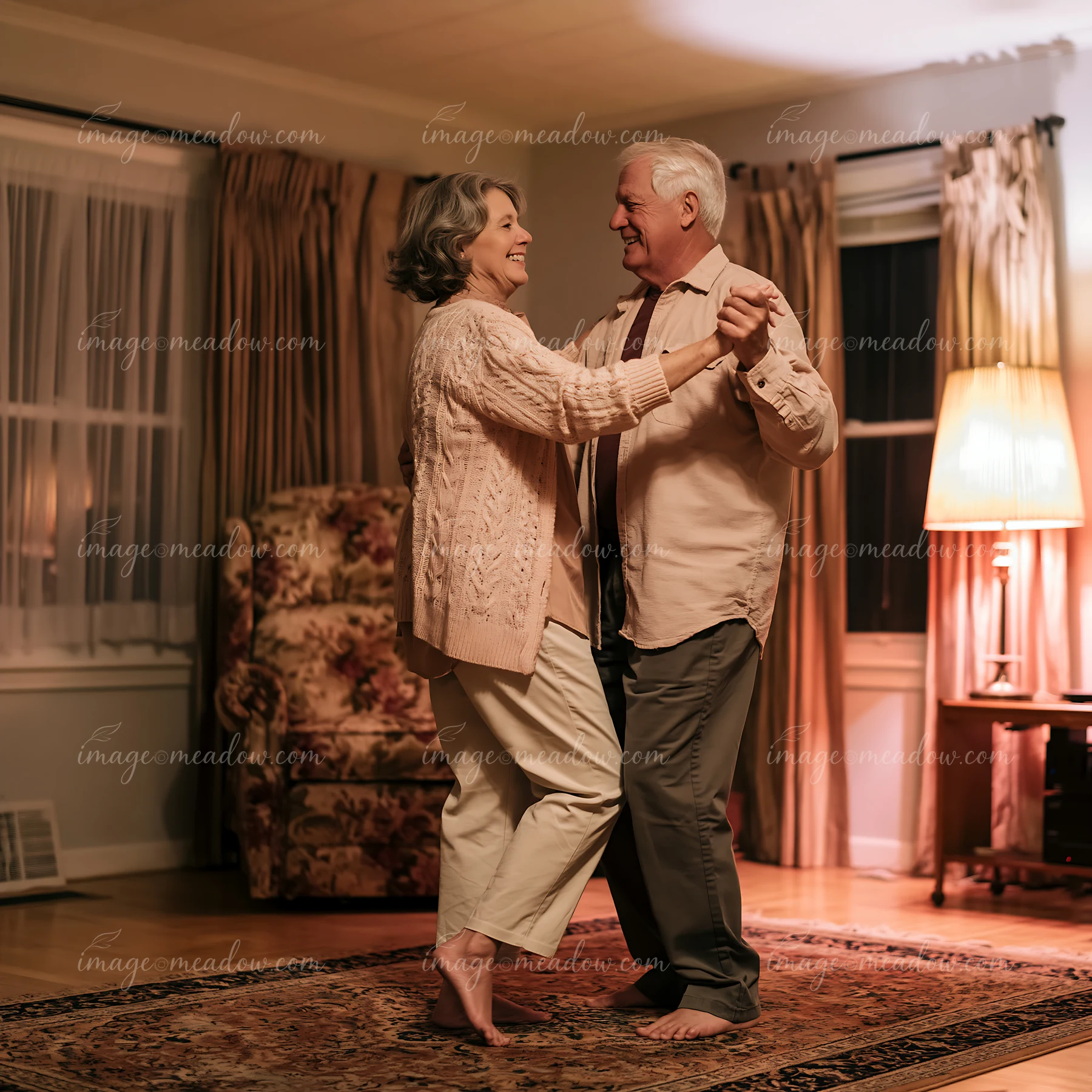 An elderly couple is dancing barefoot in a living room.