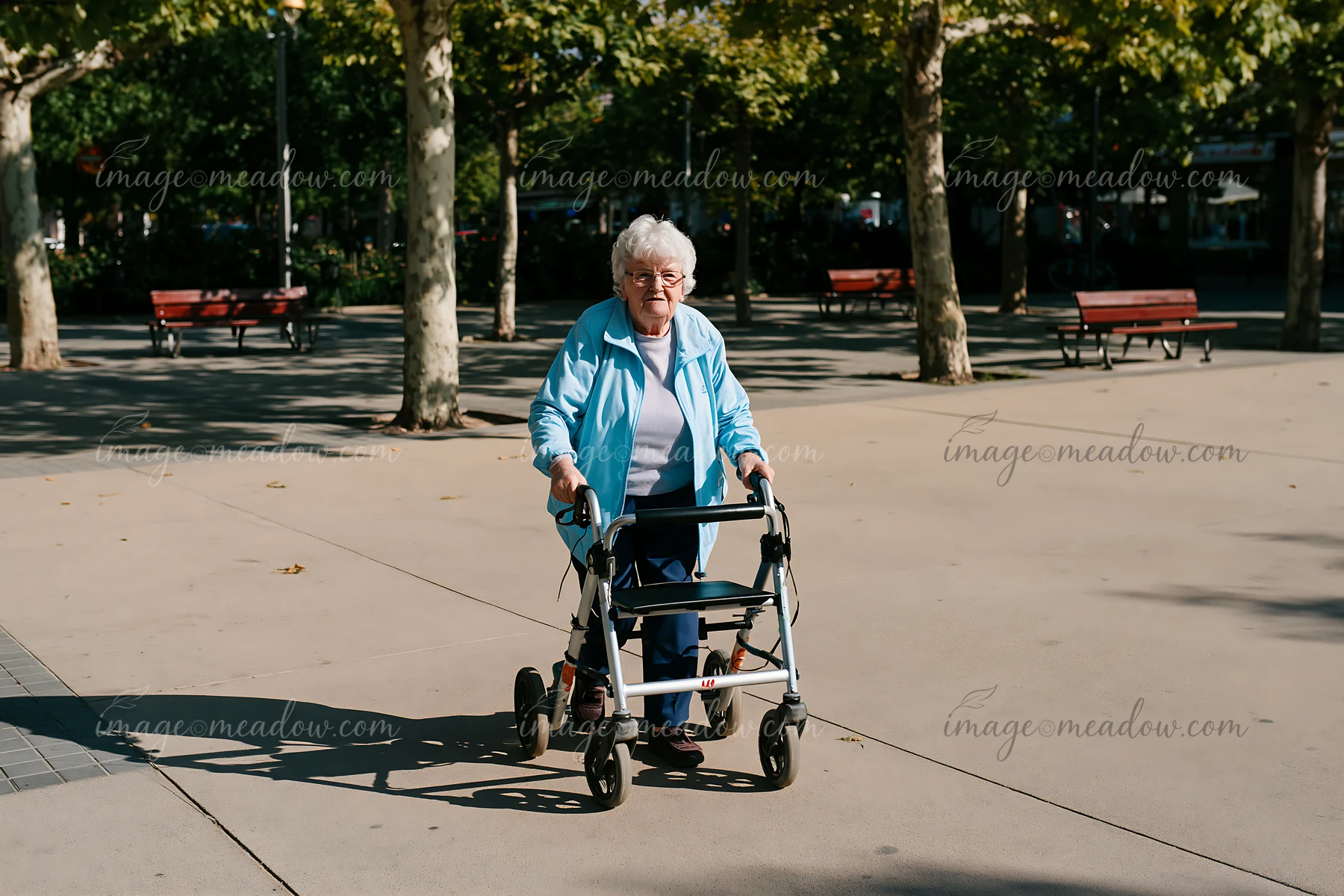 An elderly woman with Parkinson's disease walking outdoors in a park using a walker.