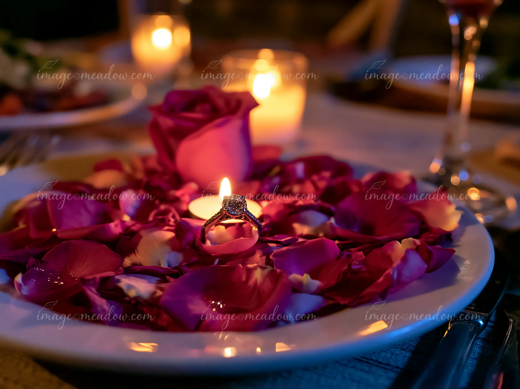 An engagement ring rests on a plate surrounded by flower petals and a candle.