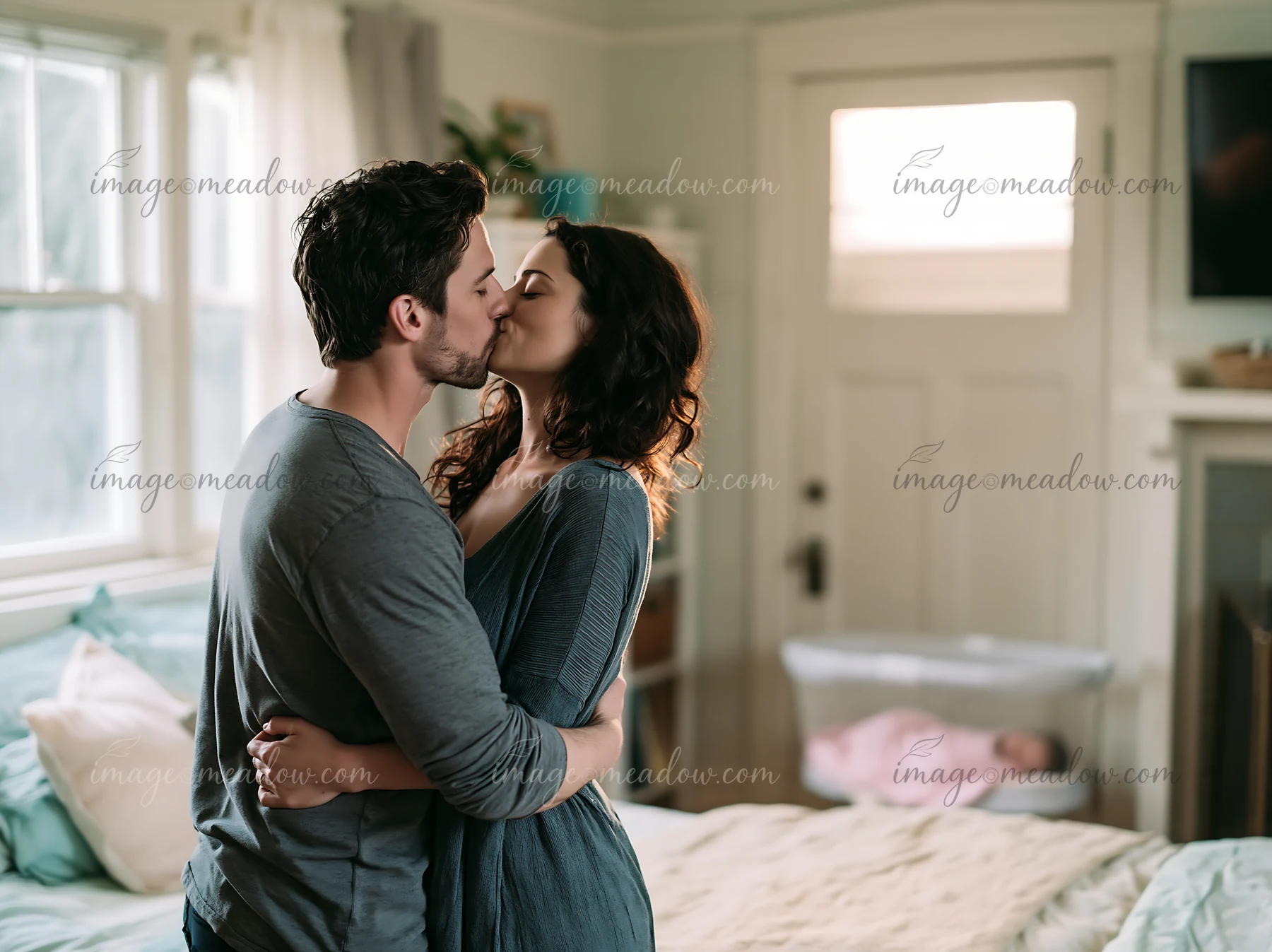 Couple kisses and embraces in a bright bedroom beside a neatly made bed.