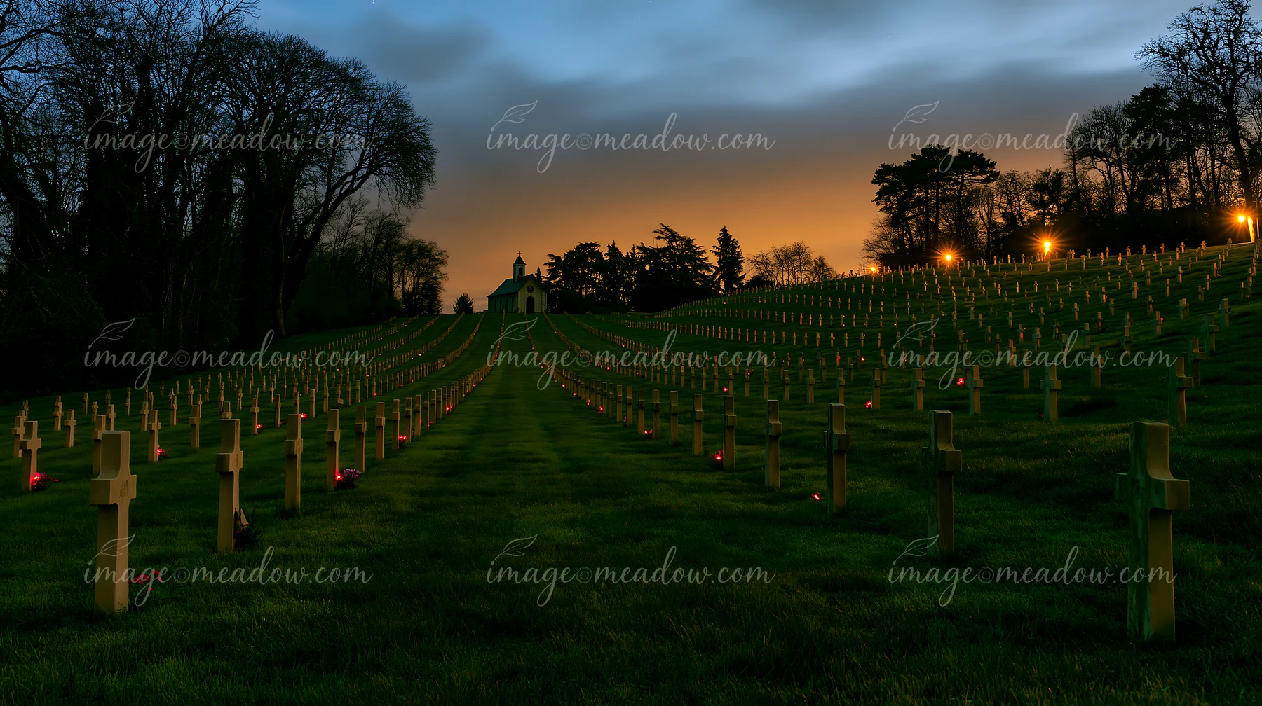 Crosses lined in rows mark a military cemetery at night, with candles illuminating the graves.