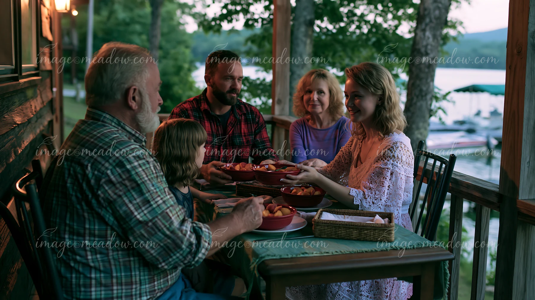 Five family members share bowls of dessert around a dinner table on a covered porch overlooking a lake.