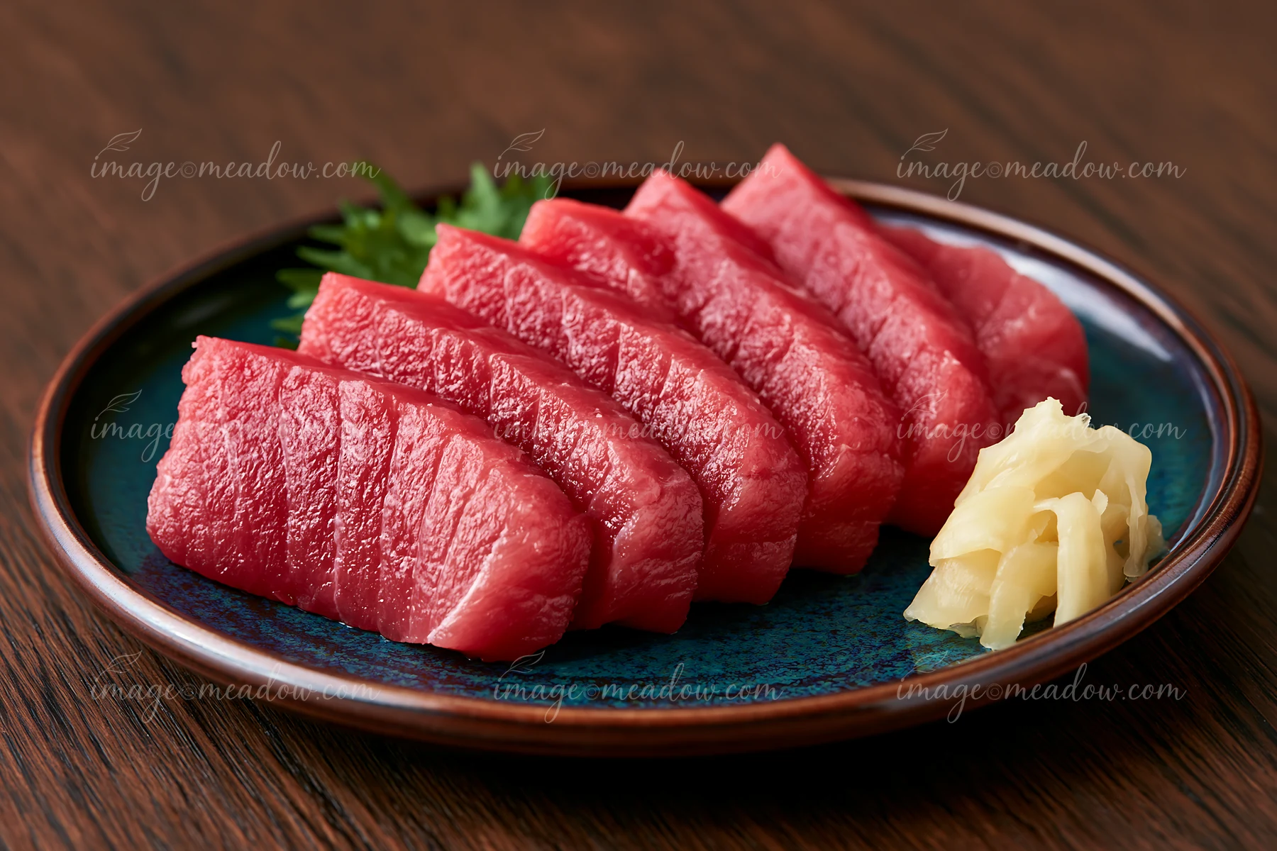 Five slices of fresh tuna are arranged neatly on a plate made of dark wood.