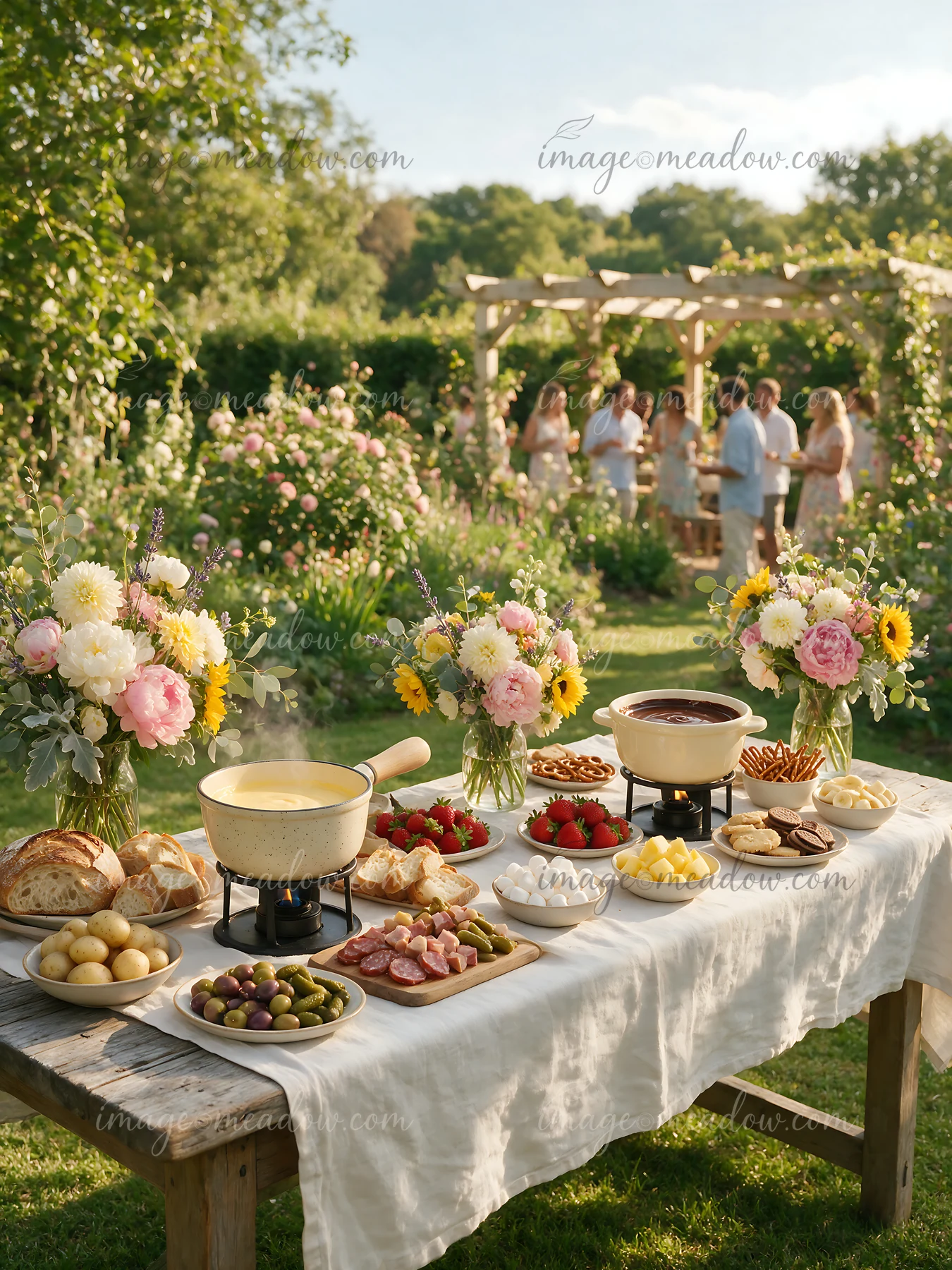 Fondue buffet table with cheese, chocolate, bread, fruit, and flowers in a sunny garden with six guests.