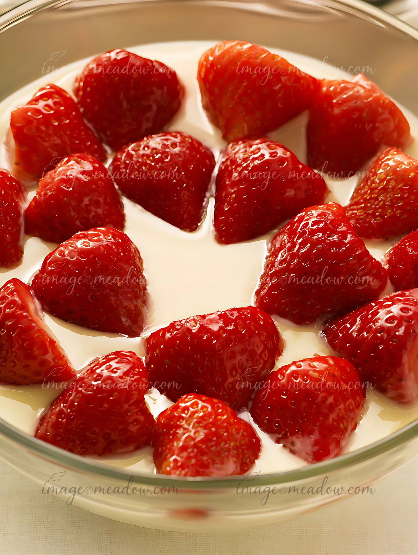 Fresh strawberries are arranged in a heart shape in a clear bowl filled with cream, presenting an attractive dessert option.