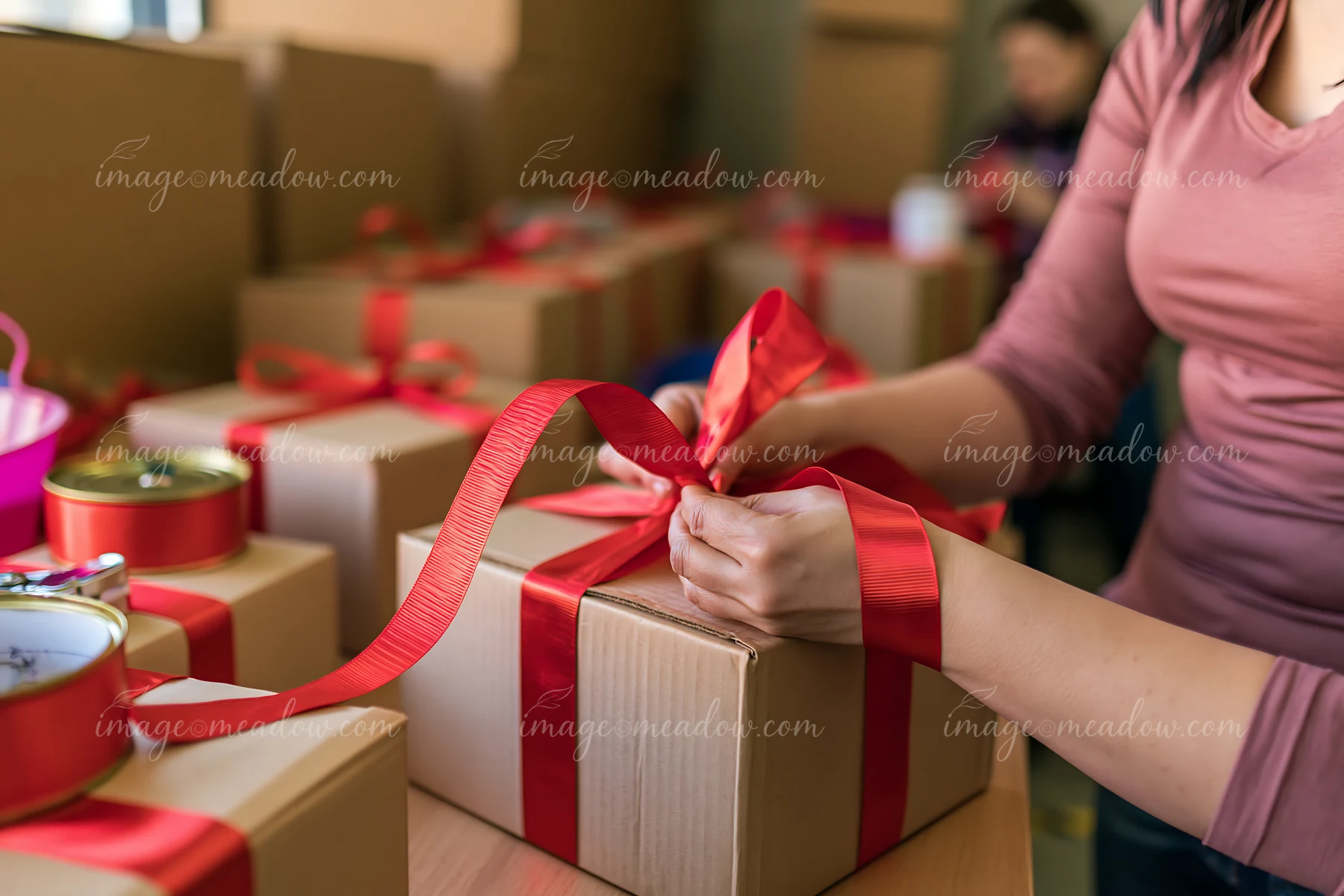 Hands are tying a red ribbon around a gift box in a wrapping station.