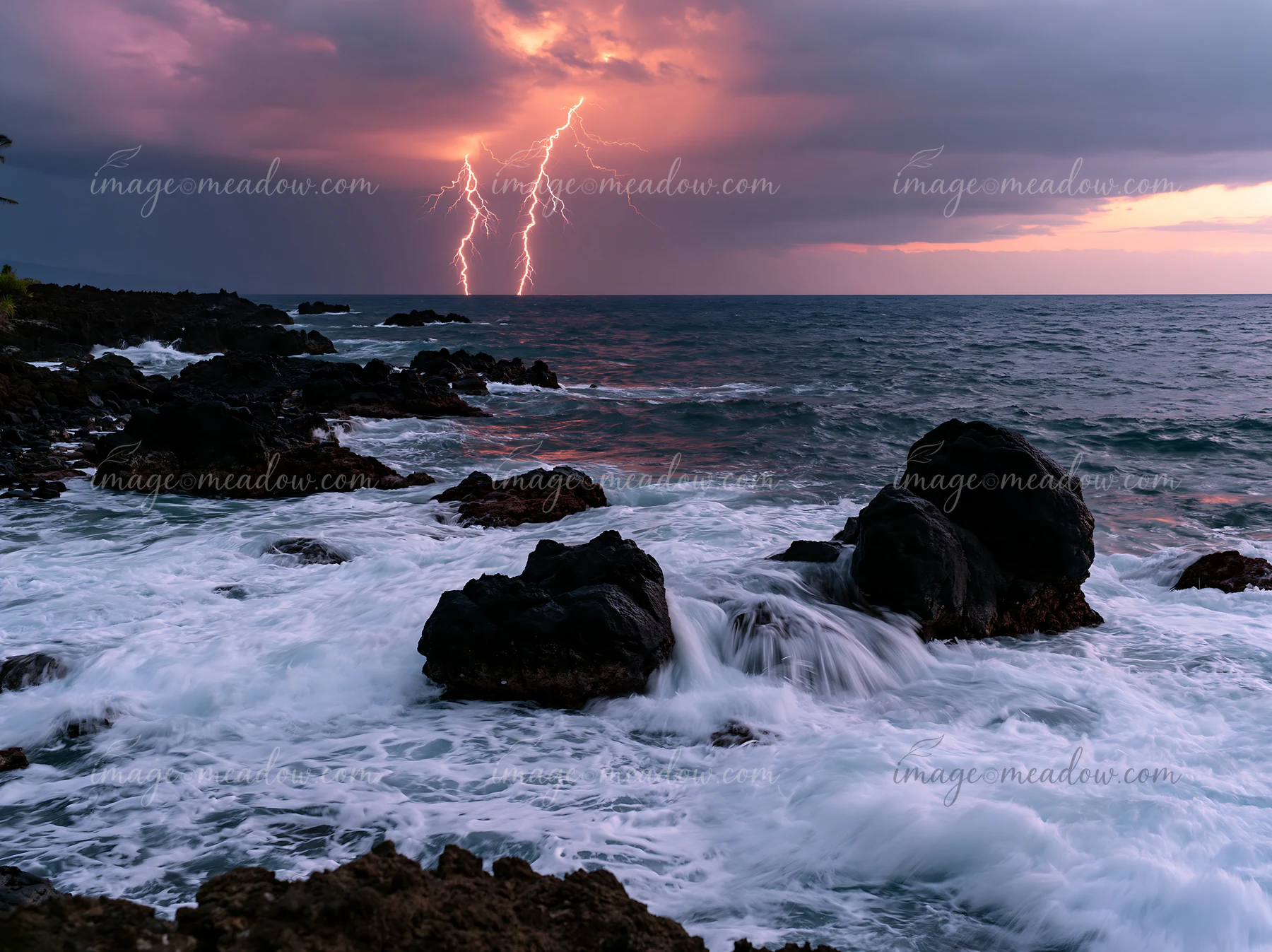 Lightning strikes illuminate the dark clouds above the coastline as waves crash against the rocky shore.