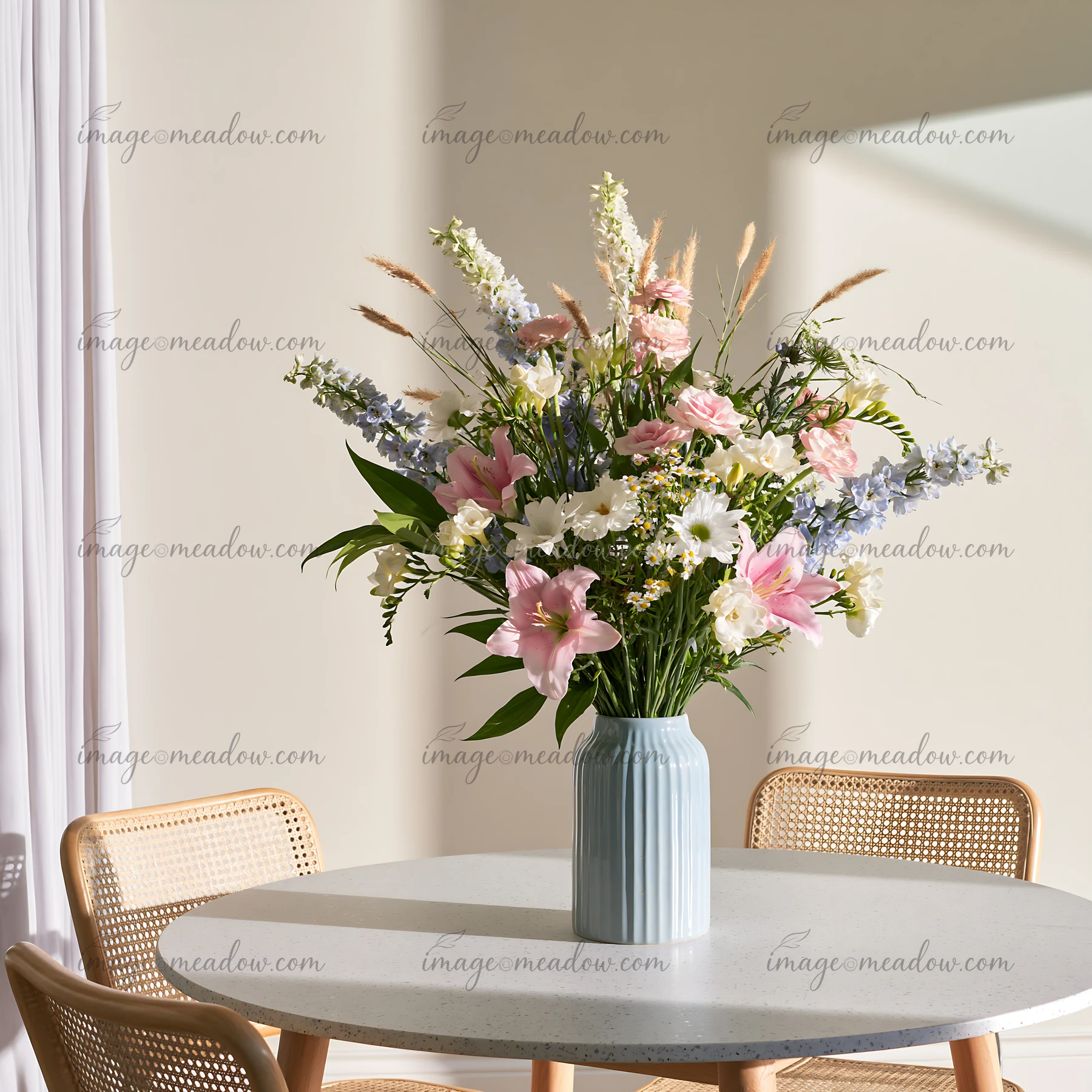 Mixed flowers in a blue ceramic vase stand on a round dining table beside woven chairs.