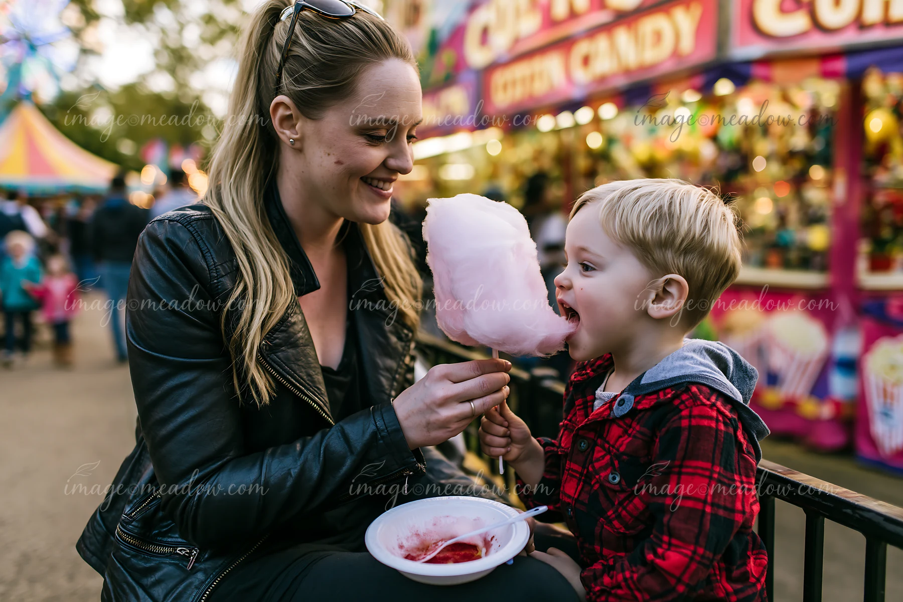 Mother and son eating cotton candy at a fair smile as they share a moment.