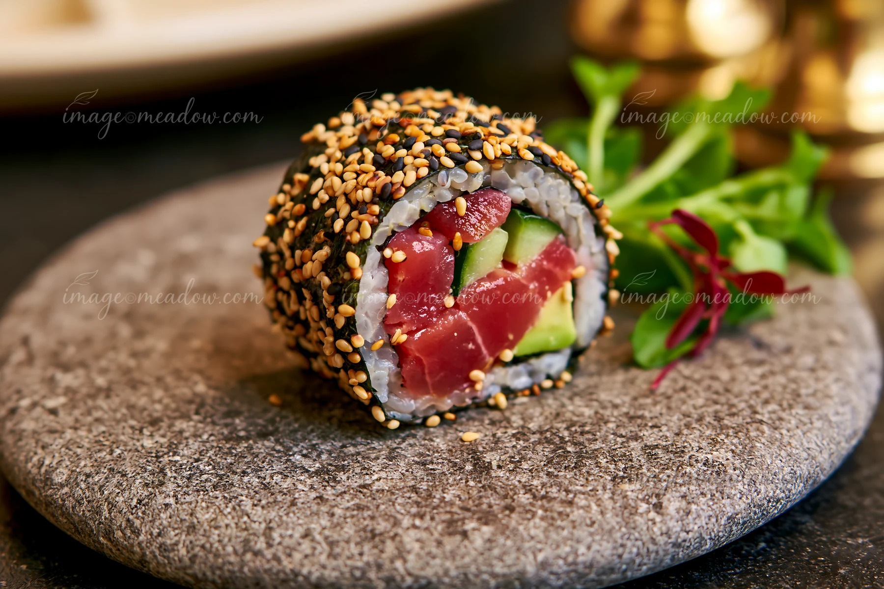 One tuna roll slice with sesame coating sits on a gray stone plate.