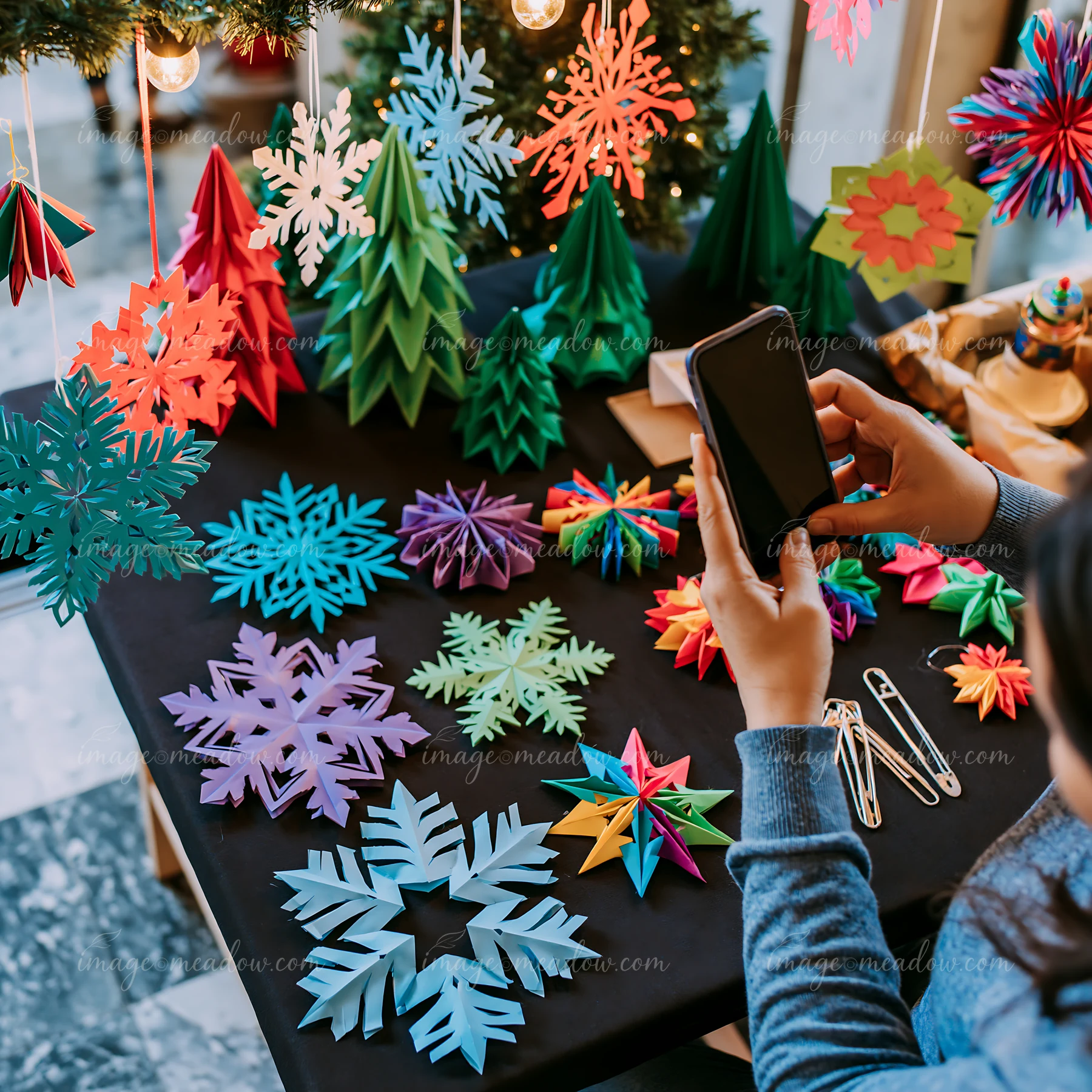 Person photographs colorful handmade paper Christmas ornaments at a festive market stall.