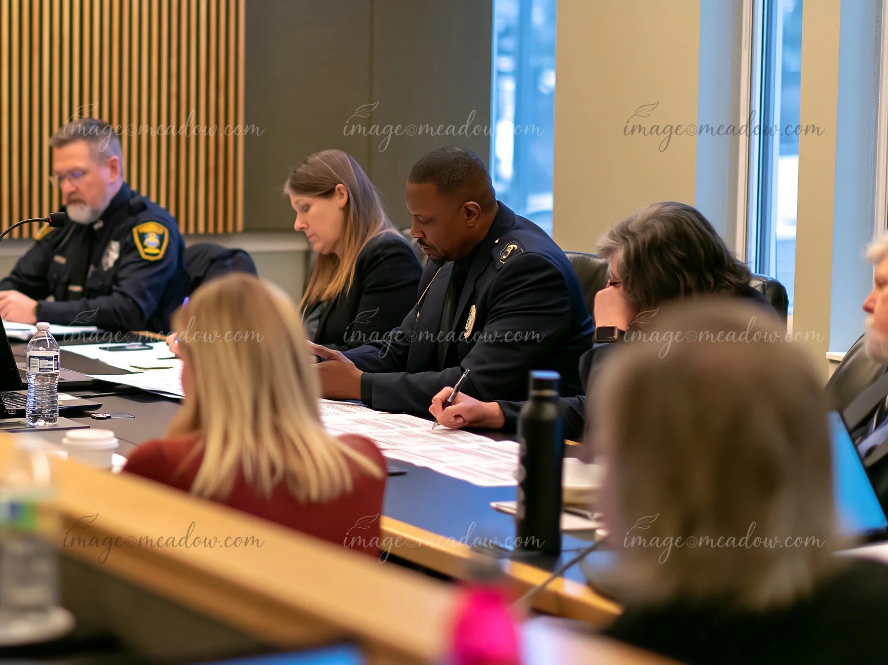Police officials and civic representatives meet around a conference table with documents and microphones.