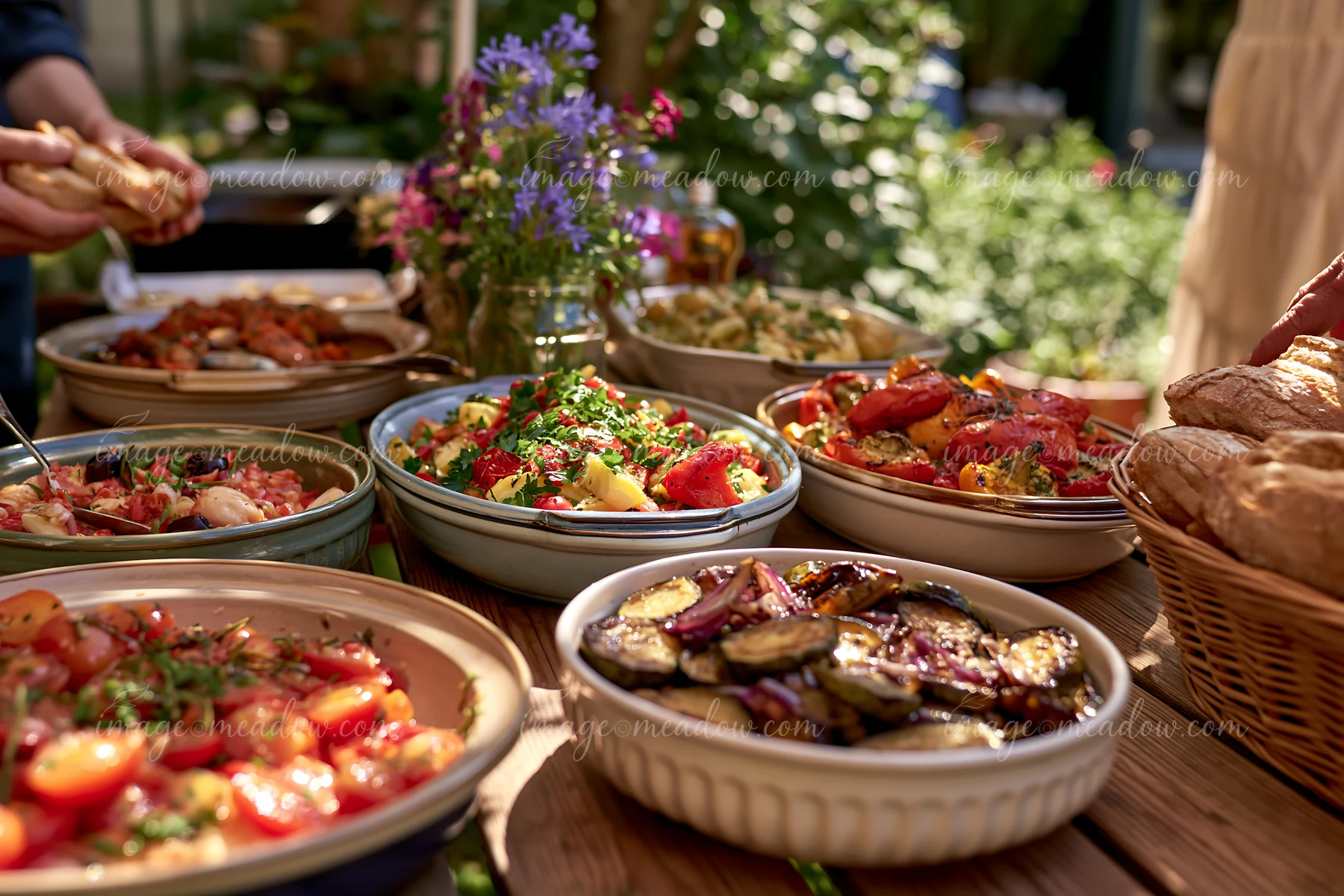 Roasted vegetables and other vegetarian dishes fill serving bowls on a sunlit outdoor buffet table.