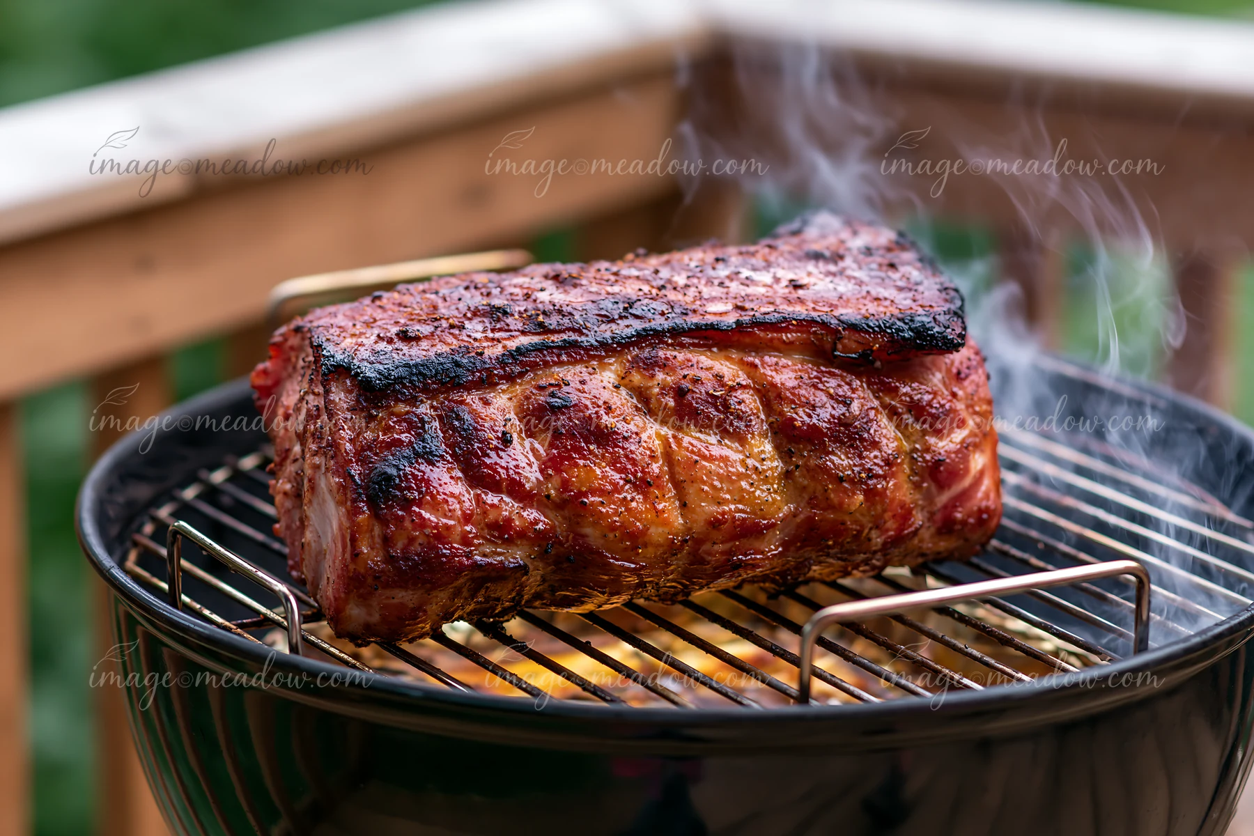 Smoke rises from a barbecue grill where a whole roast pork is cooking on an outdoor deck.