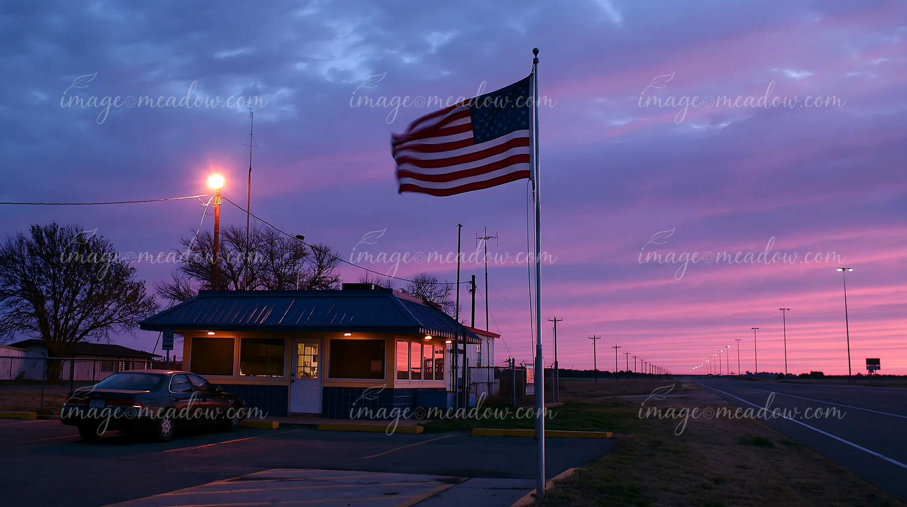 The American flag flying in strong wind is displayed at a roadside shelter during twilight.