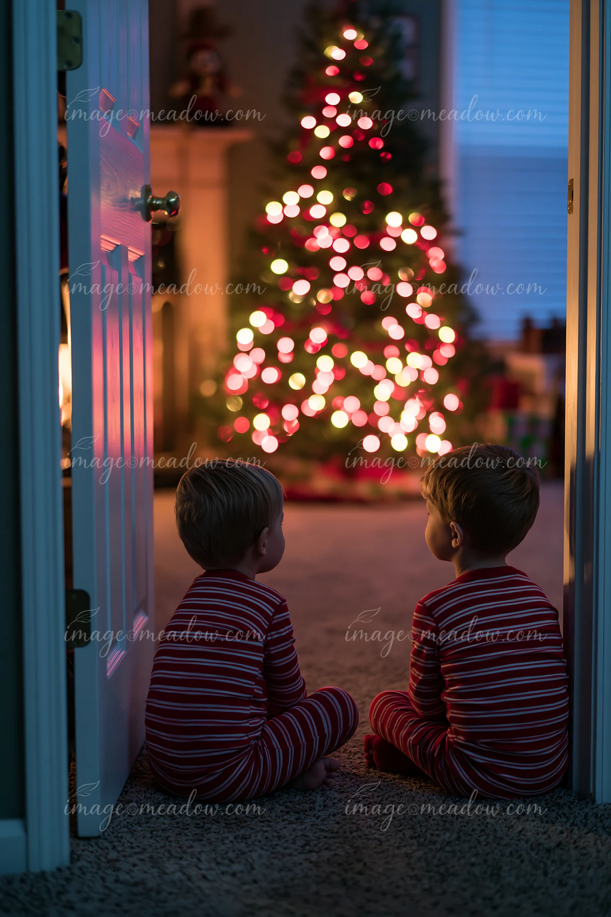 Two children wear matching pajamas while sitting on a carpet in front of a Christmas tree.