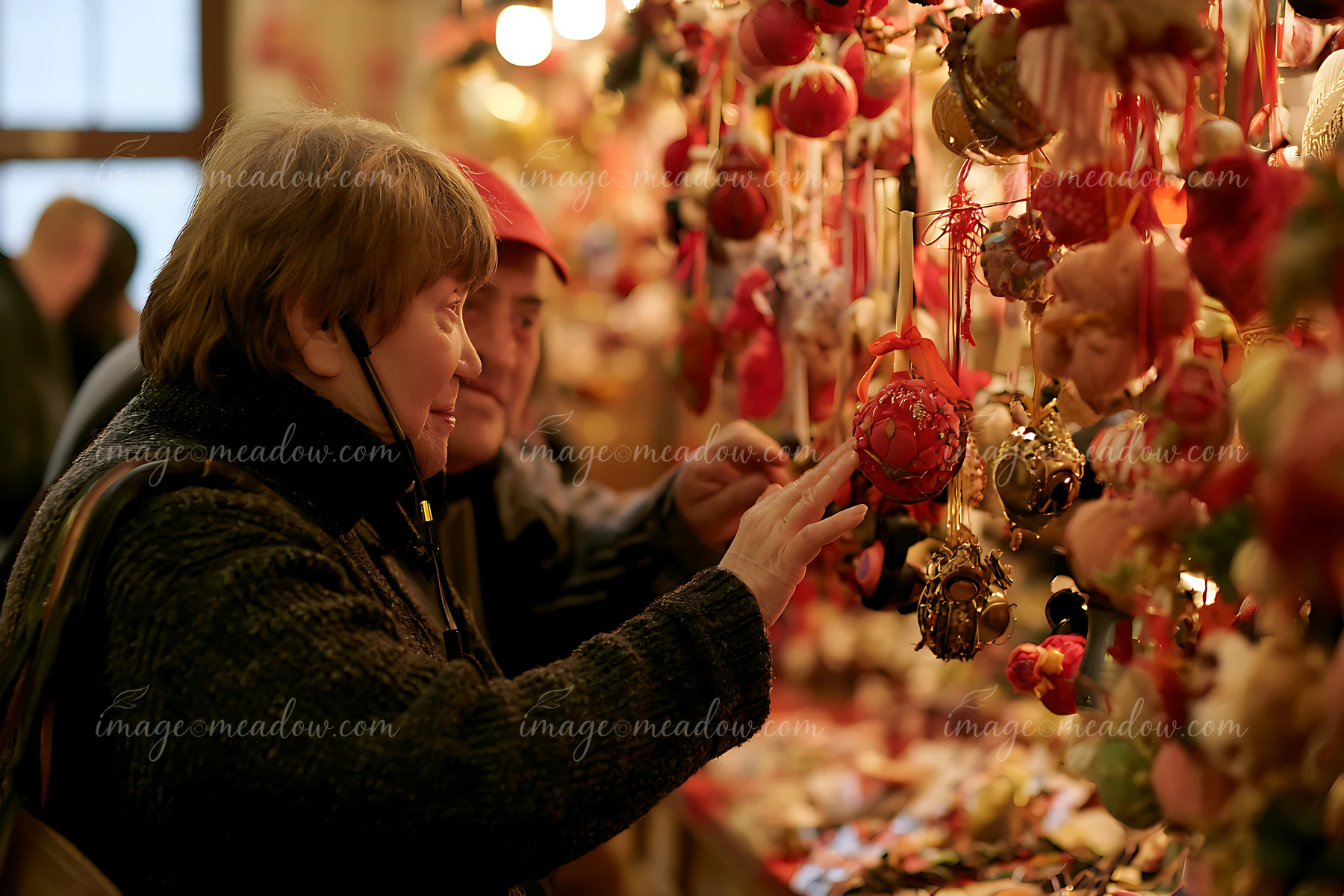 Two customers admire and choose handmade ornaments at a Christmas market stall.