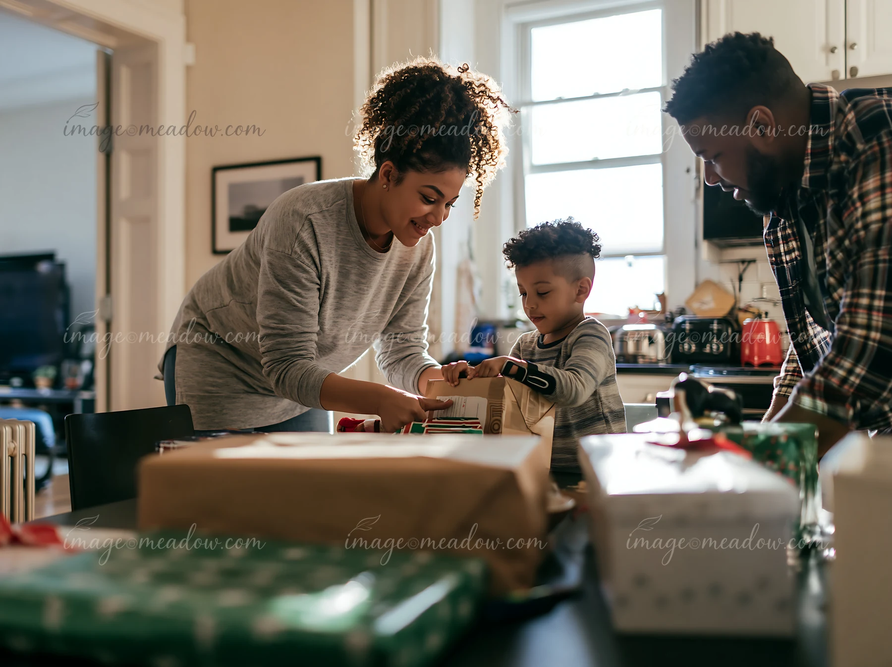 Two parents and their child wrap gifts together at a dining table in a bright home kitchen.