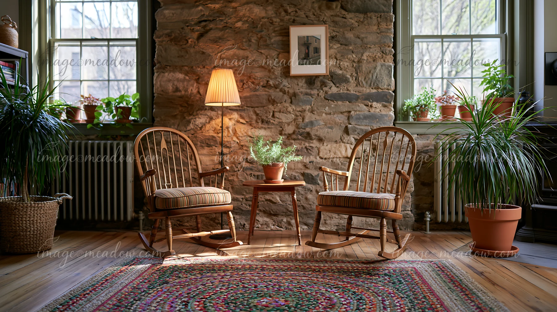 Two rocking chairs sit beside a small table under a lamp in a room featuring an exposed stone wall.