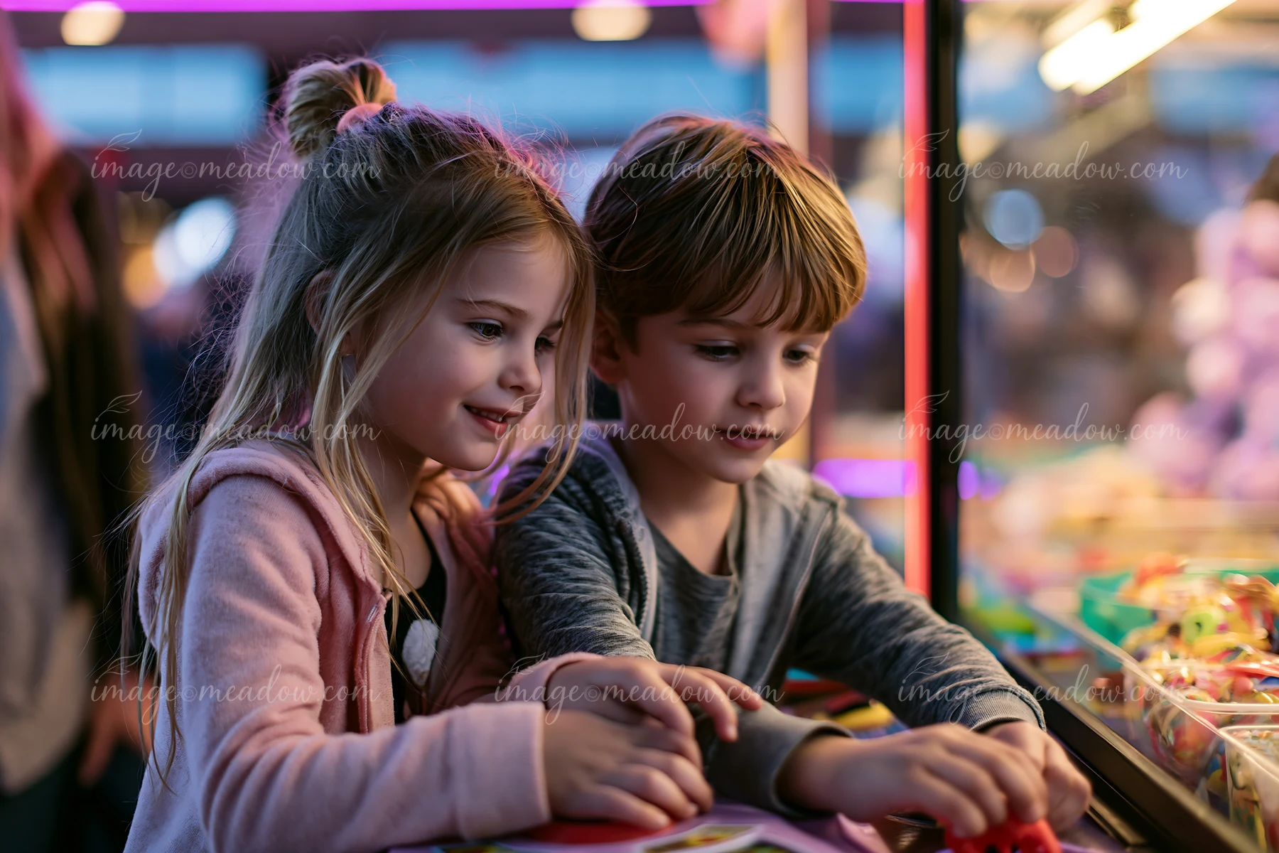 Two siblings playing a claw-style prize game at a fun fair.