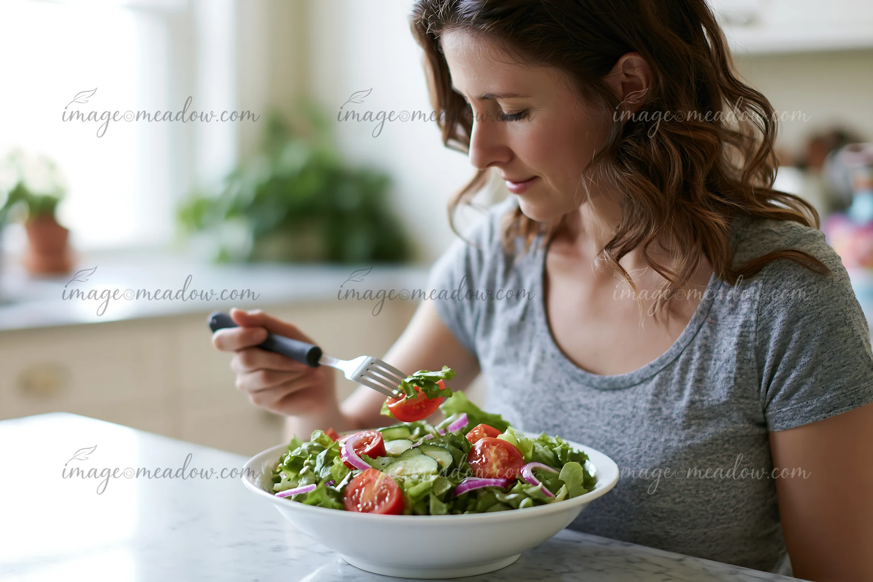 Woman with limited hand mobility uses a fork to eat salad at a bright kitchen table.