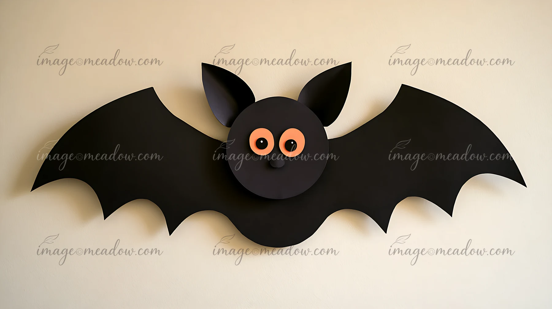 A bat decoration hangs on a wall, featuring a rounded black body, large pointed ears, and orange eyes.