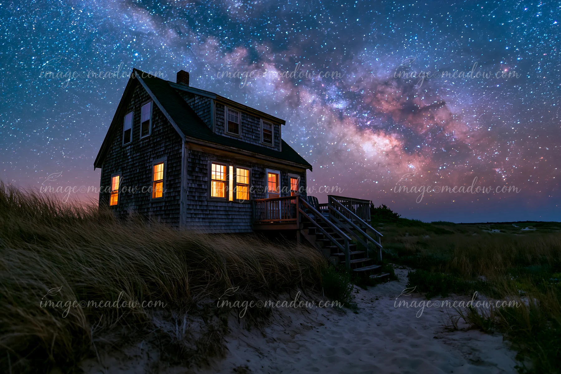 A beach house stands near sand dunes under a starry sky with the Milky Way visible.