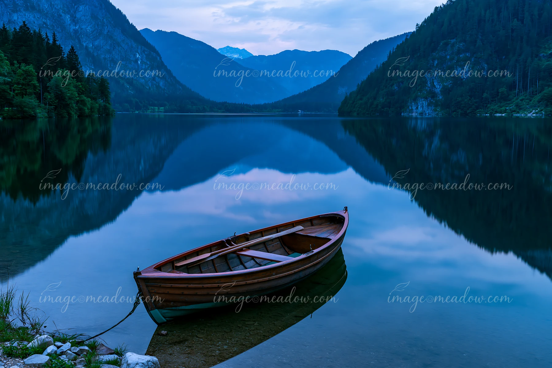 A boat is moored at the edge of an alpine lake, which reflects the surrounding mountains and trees.