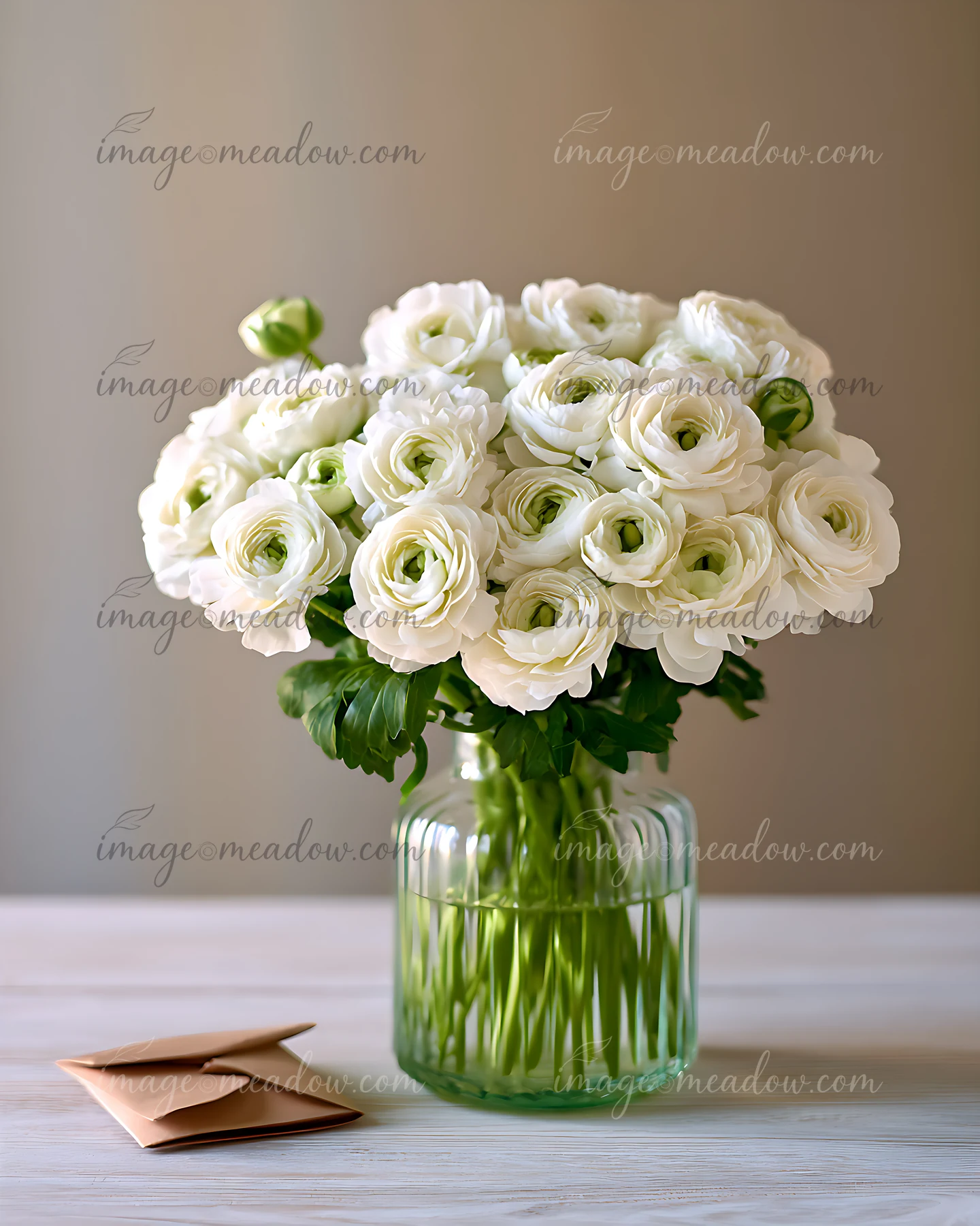 A bouquet of white ranunculus flowers sits in a clear glass vase on a wooden table.
