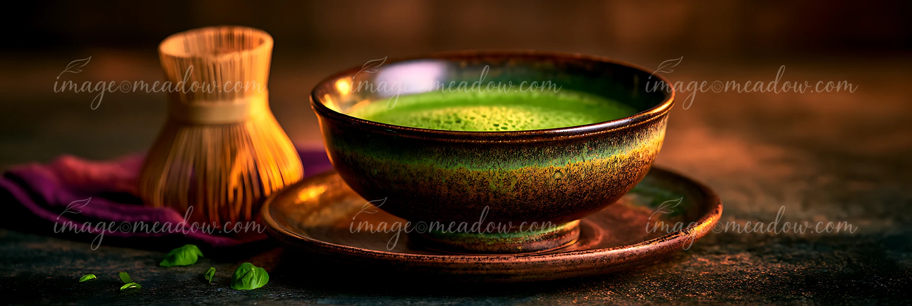 A bowl of green matcha tea sits on a dark surface next to a bamboo whisk.