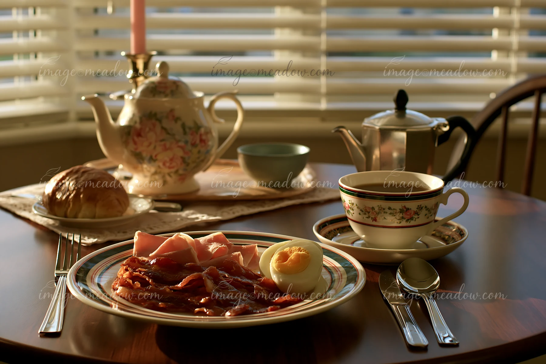 A breakfast plate with cold cuts, boiled egg, and a roll sits on a wooden table by a window.