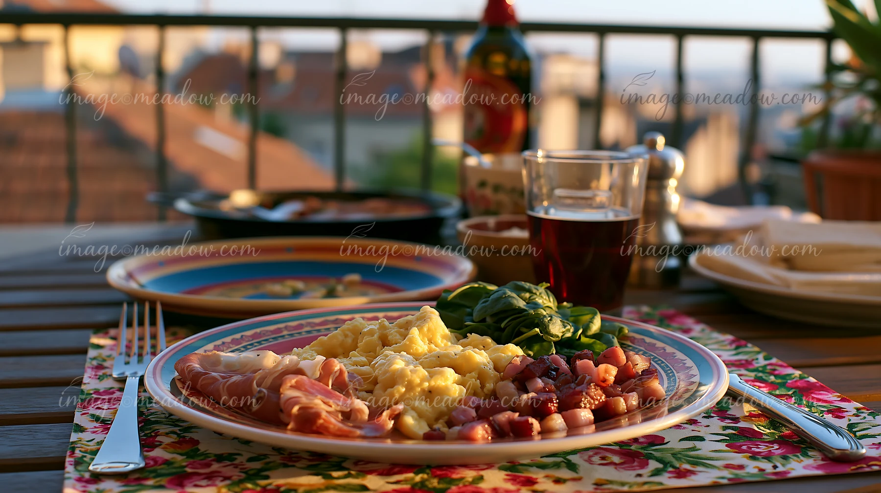 A breakfast plate with cold cuts sits on a wooden table with a view of the city.