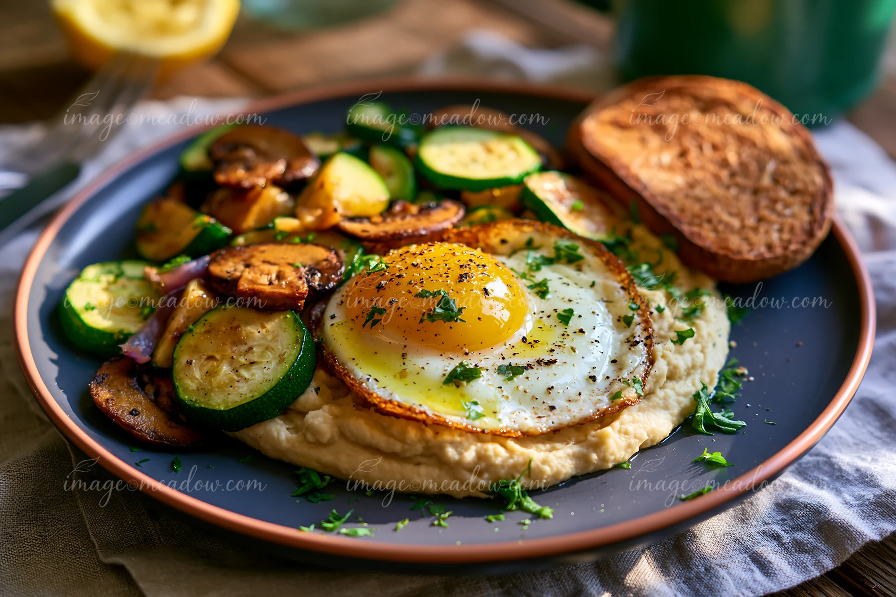 A breakfast plate with hummus, a fried egg on top, and sautéed zucchini and mushrooms.