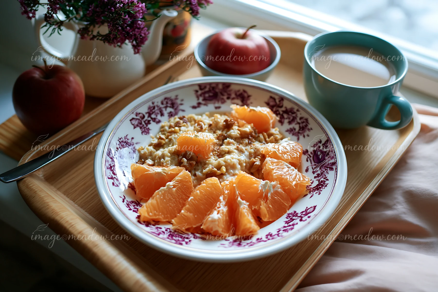 A breakfast plate with muesli is served with orange slices, an apple, and a cup of milk on a wooden tray.