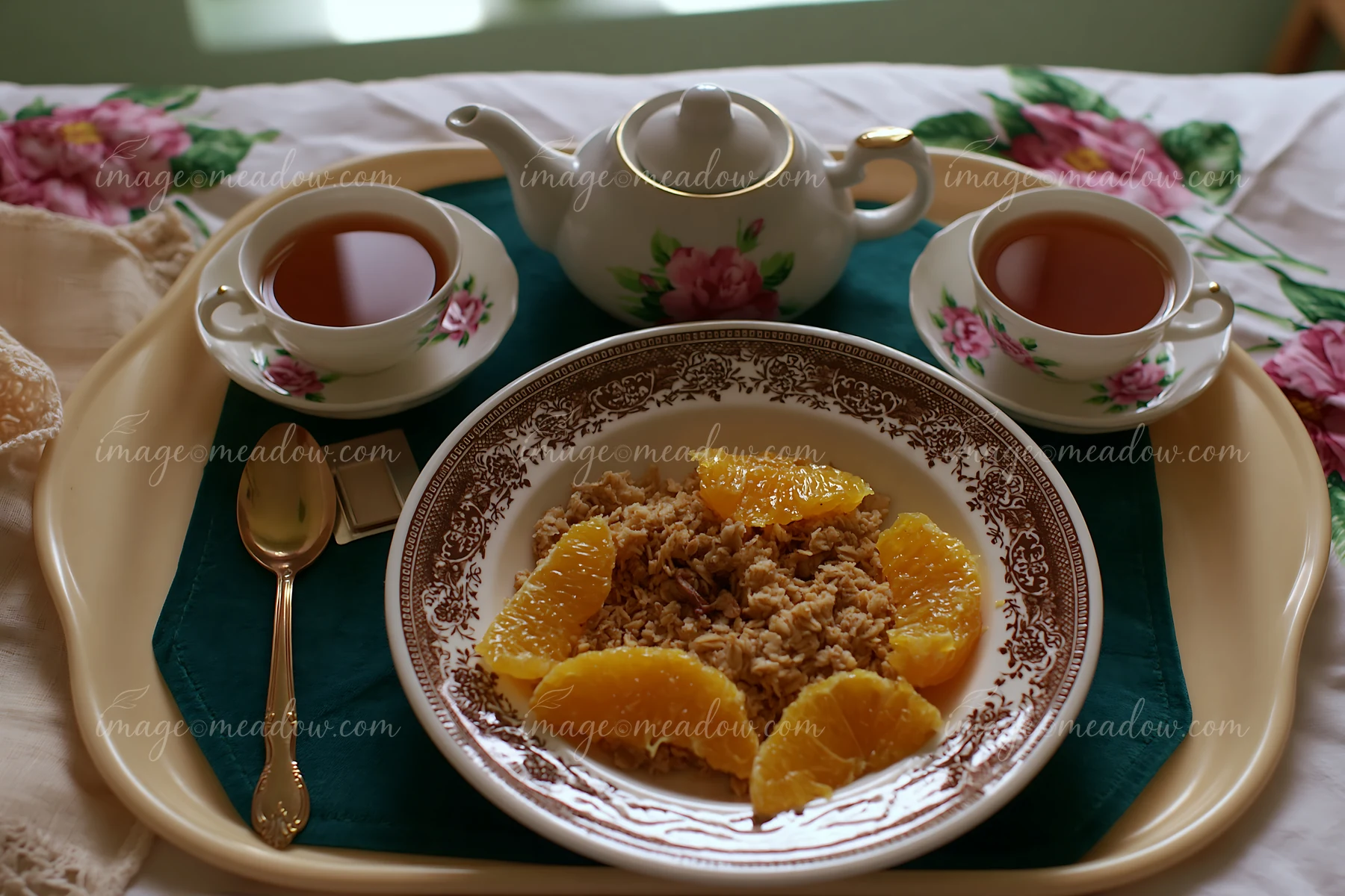 A breakfast plate with muesli topped with orange slices sits on a tray with two cups of tea.