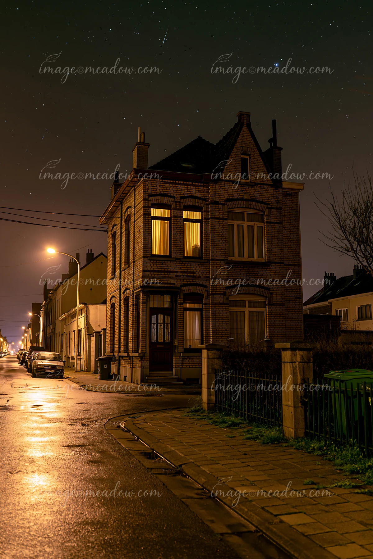 A brick house stands in a quiet neighborhood as a meteor shower illuminates the night sky.