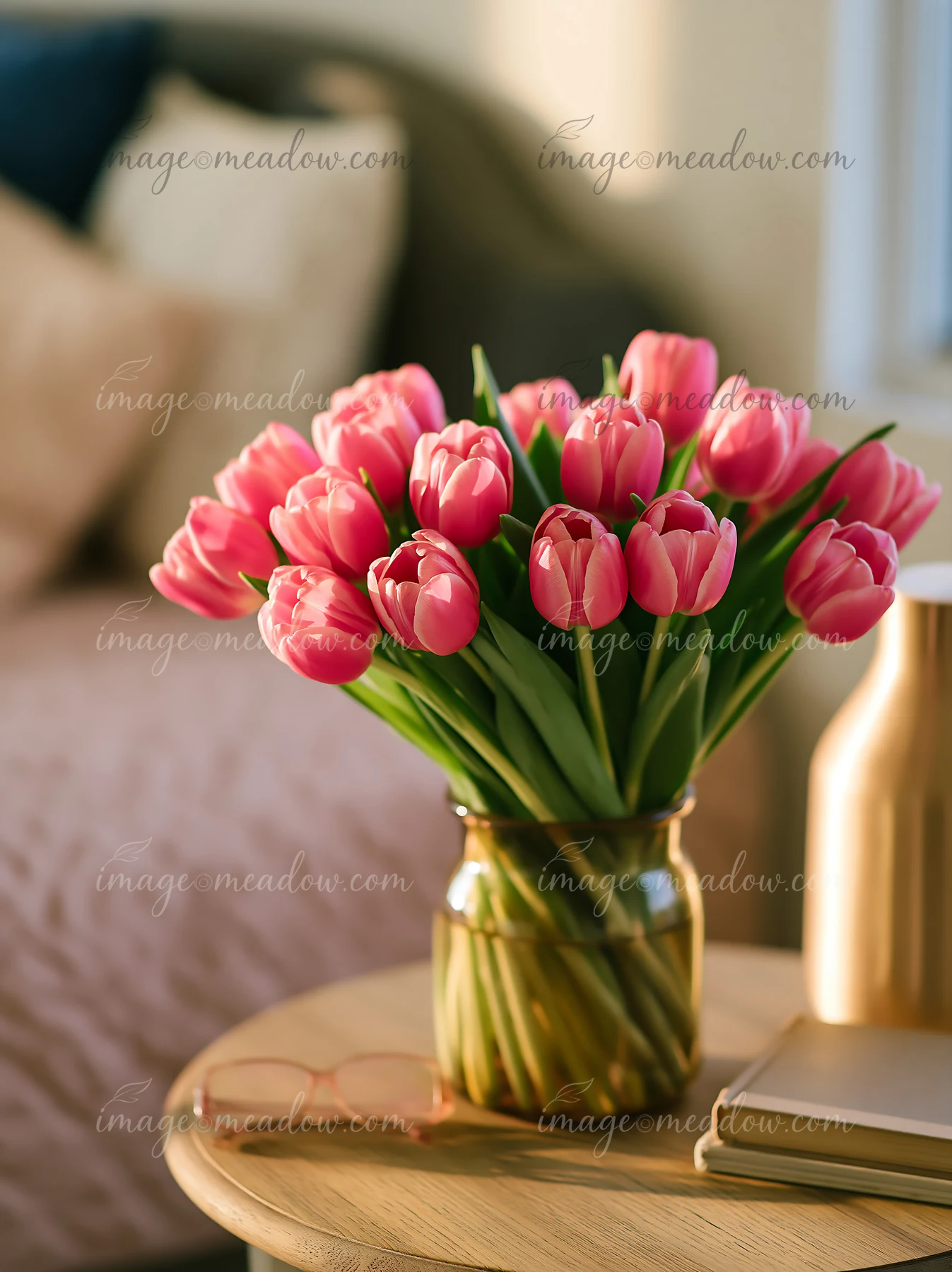A bunch of pink tulips in a jar sits on a bedside table.