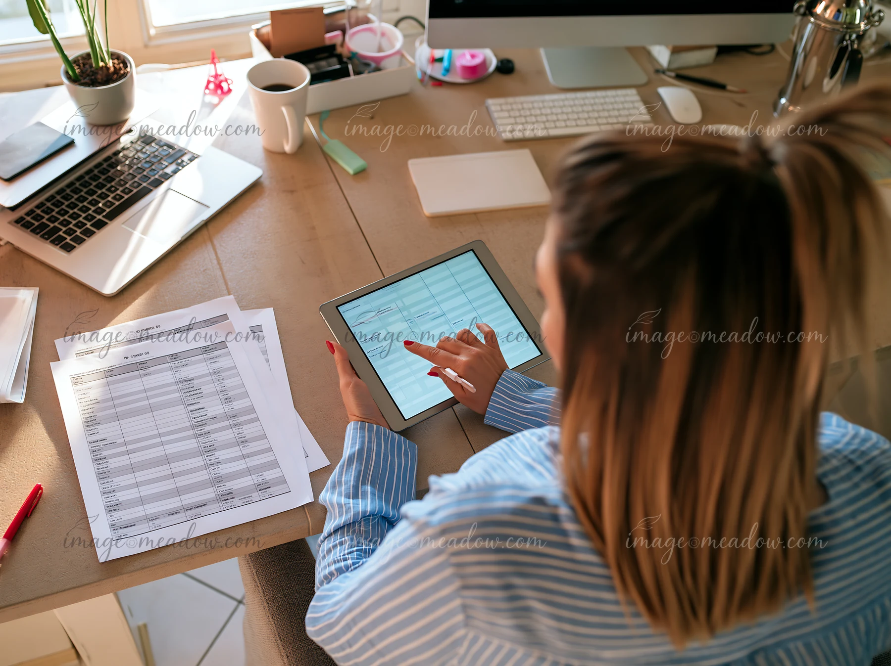 A businesswoman uses a tablet to manage a project timeline at her desk.