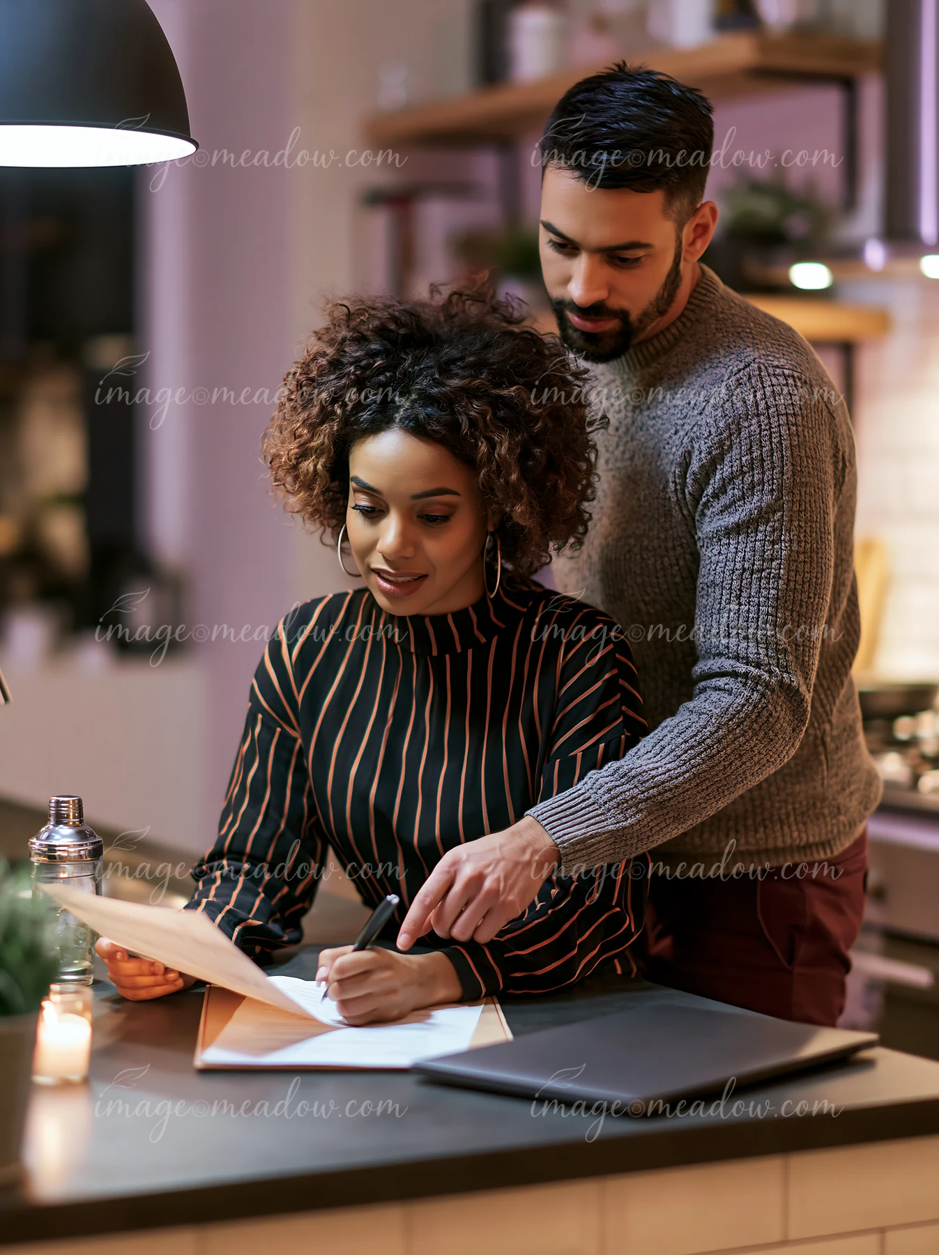 A businesswoman writes on a document while an advisor points to details in a stylish kitchen.