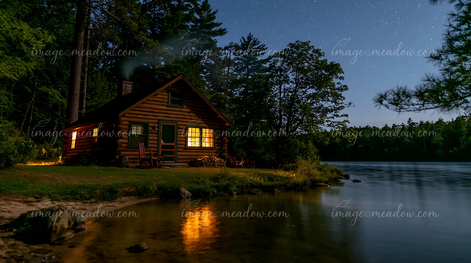 A cabin with smoke rising under stars sits by a lake surrounded by trees.