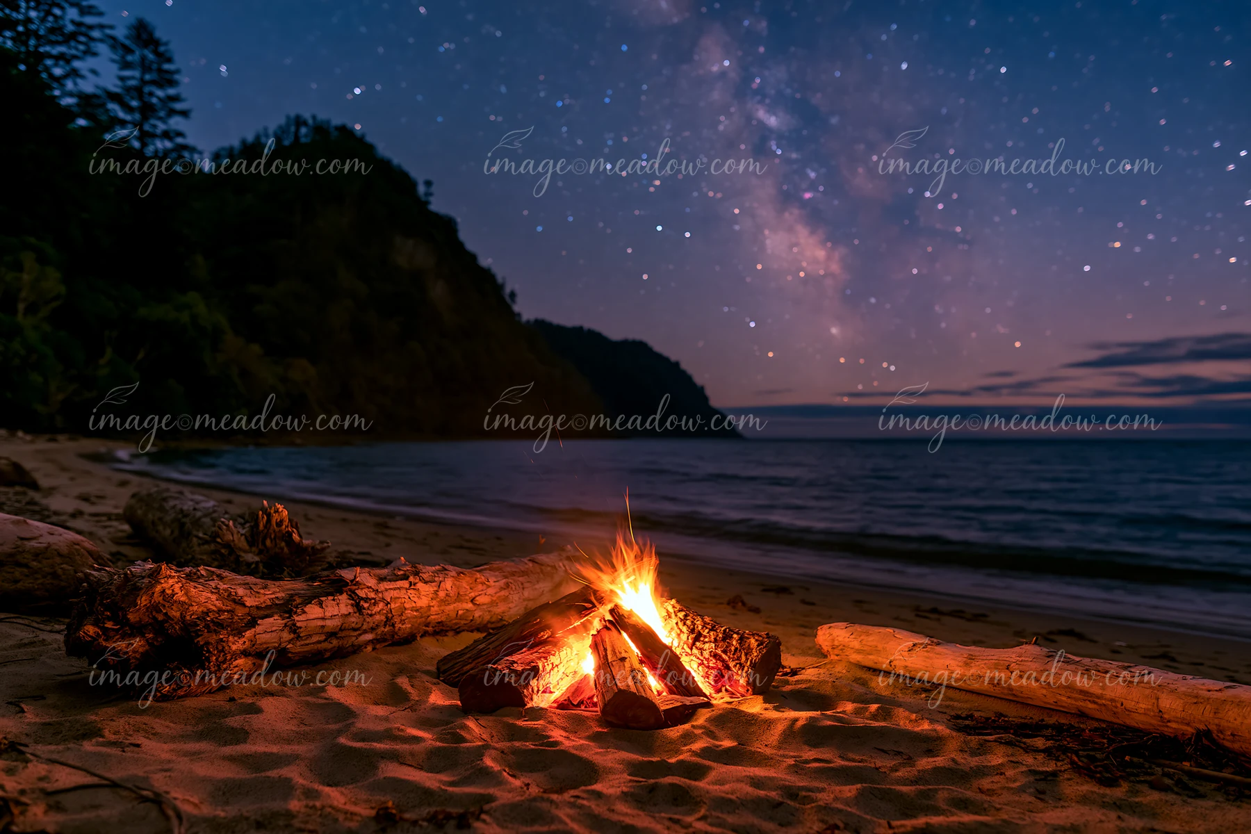A campfire glows on the sand of a secluded beach while stars fill the night sky over a calm ocean.