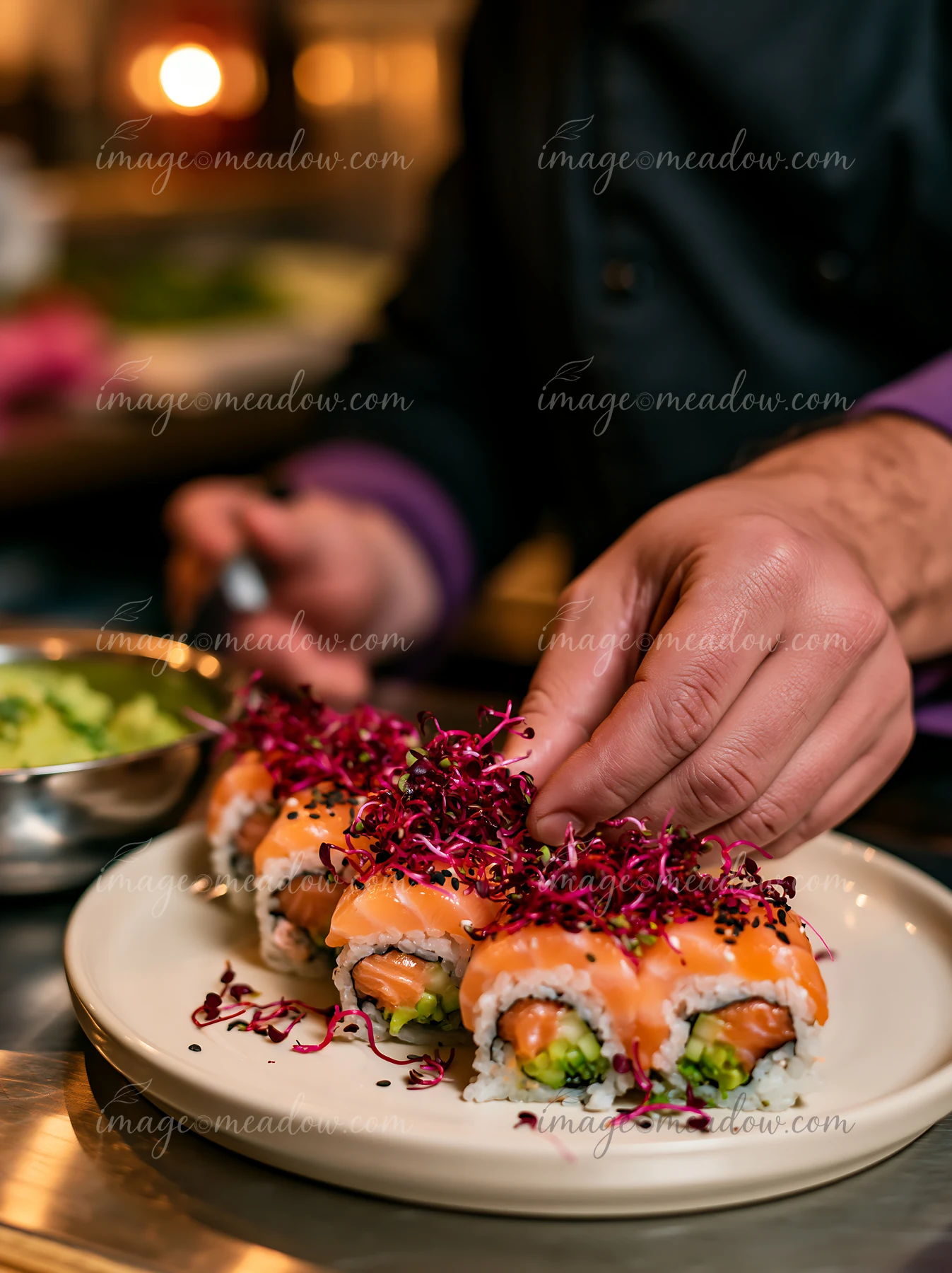 A chef adds microgreens on top of sushi rolls in a restaurant kitchen.
