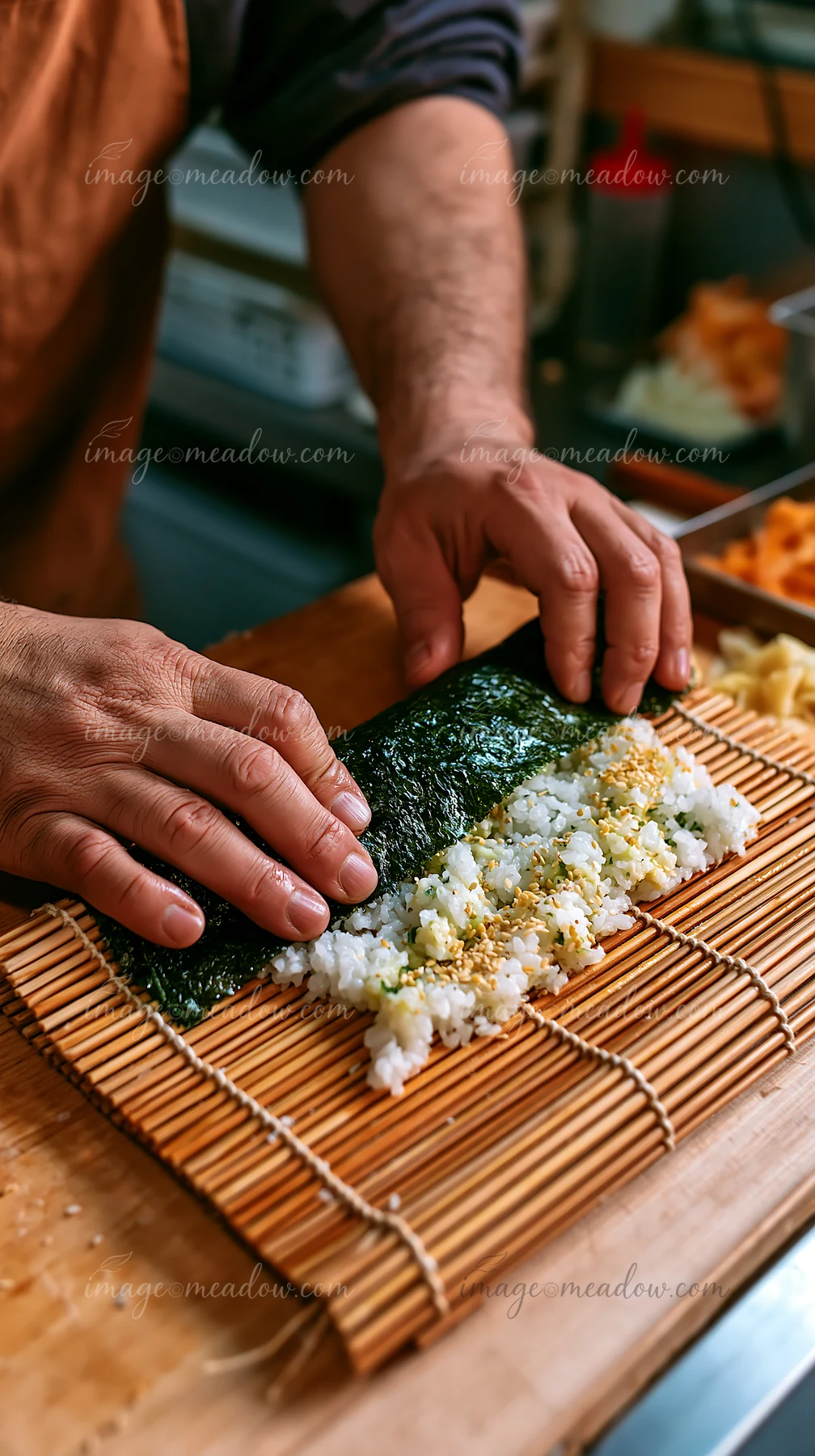 A chef prepares sushi wrapped in nori seaweed using fresh ingredients on a bamboo mat.