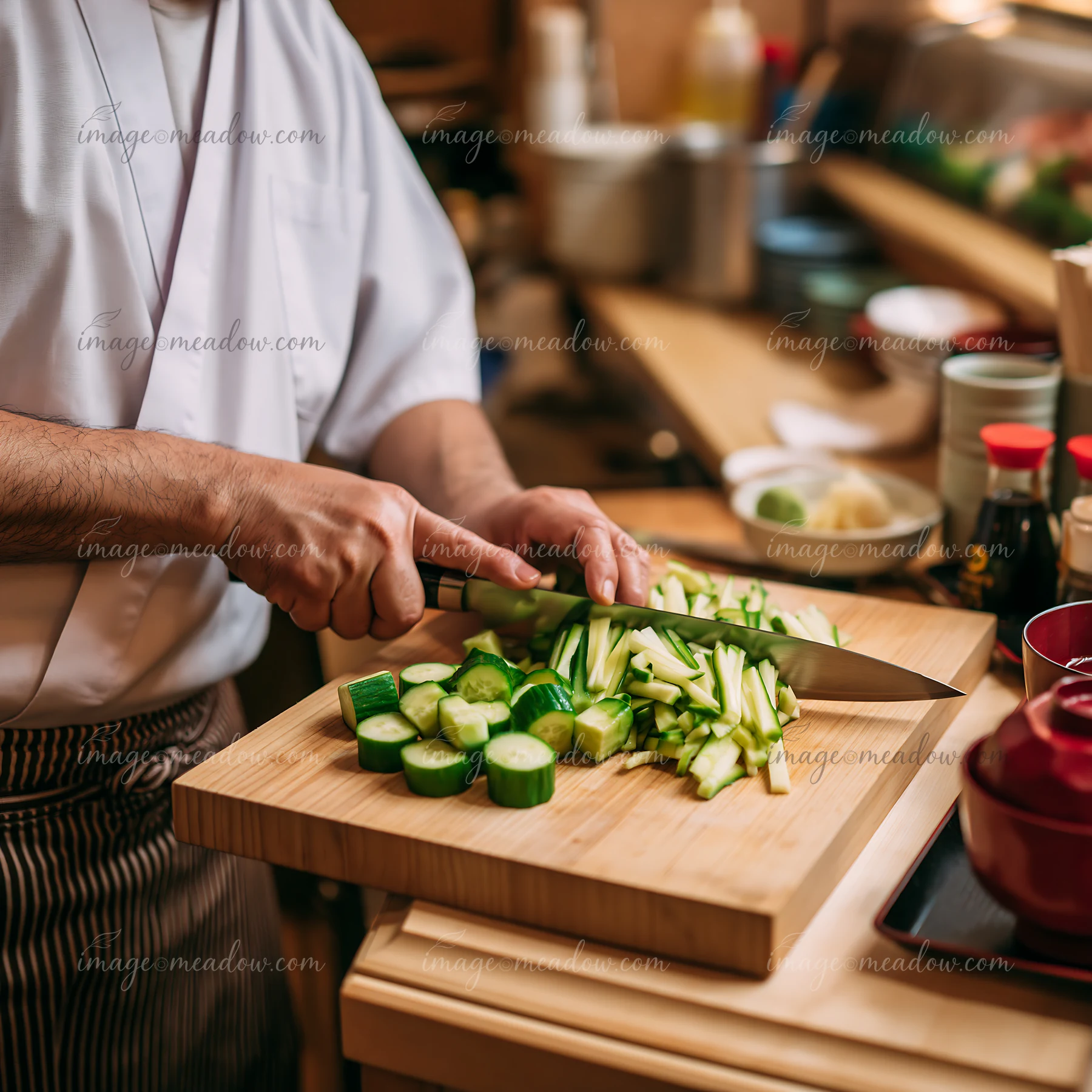 A chef preparing sushi at restaurant counter slices cucumbers on a wooden cutting board.