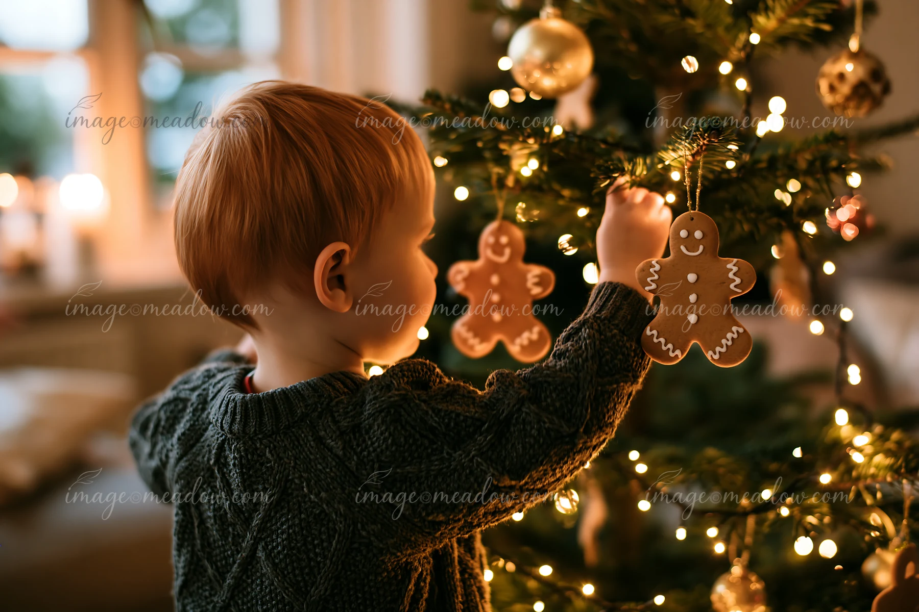 A child hangs gingerbread ornaments on a Christmas tree in a cozy living room with warm lighting.