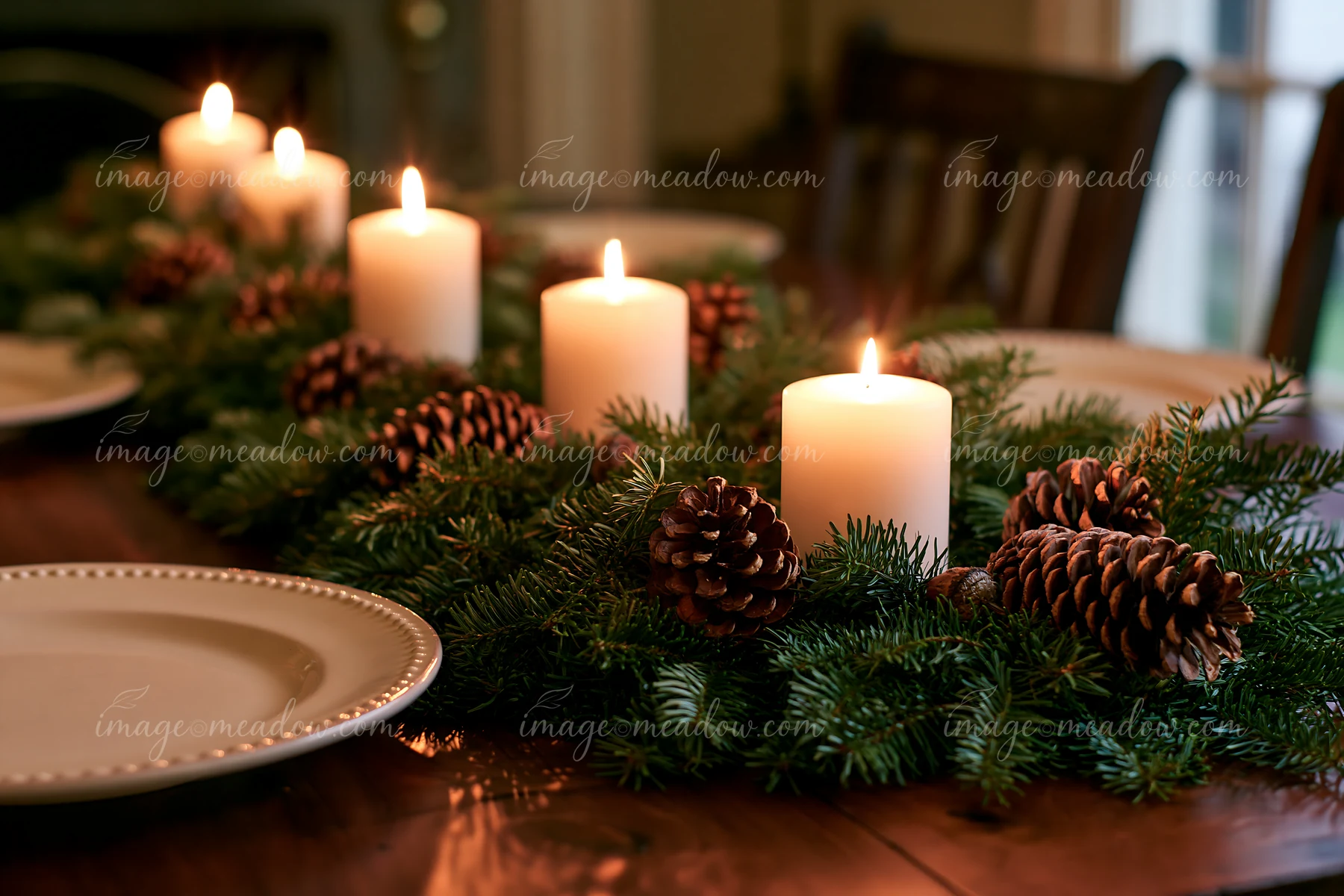 A Christmas centerpiece features lit candles and pinecones arranged on a table with empty dining plates.