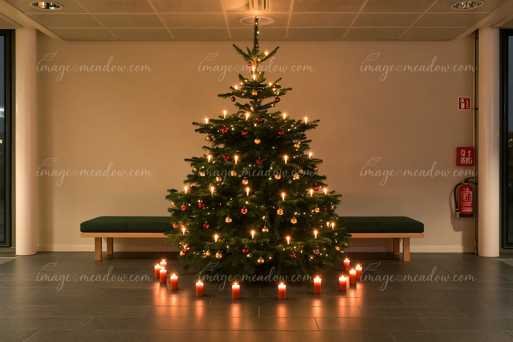 A Christmas tree with candles nearby stands in a bright indoor space.