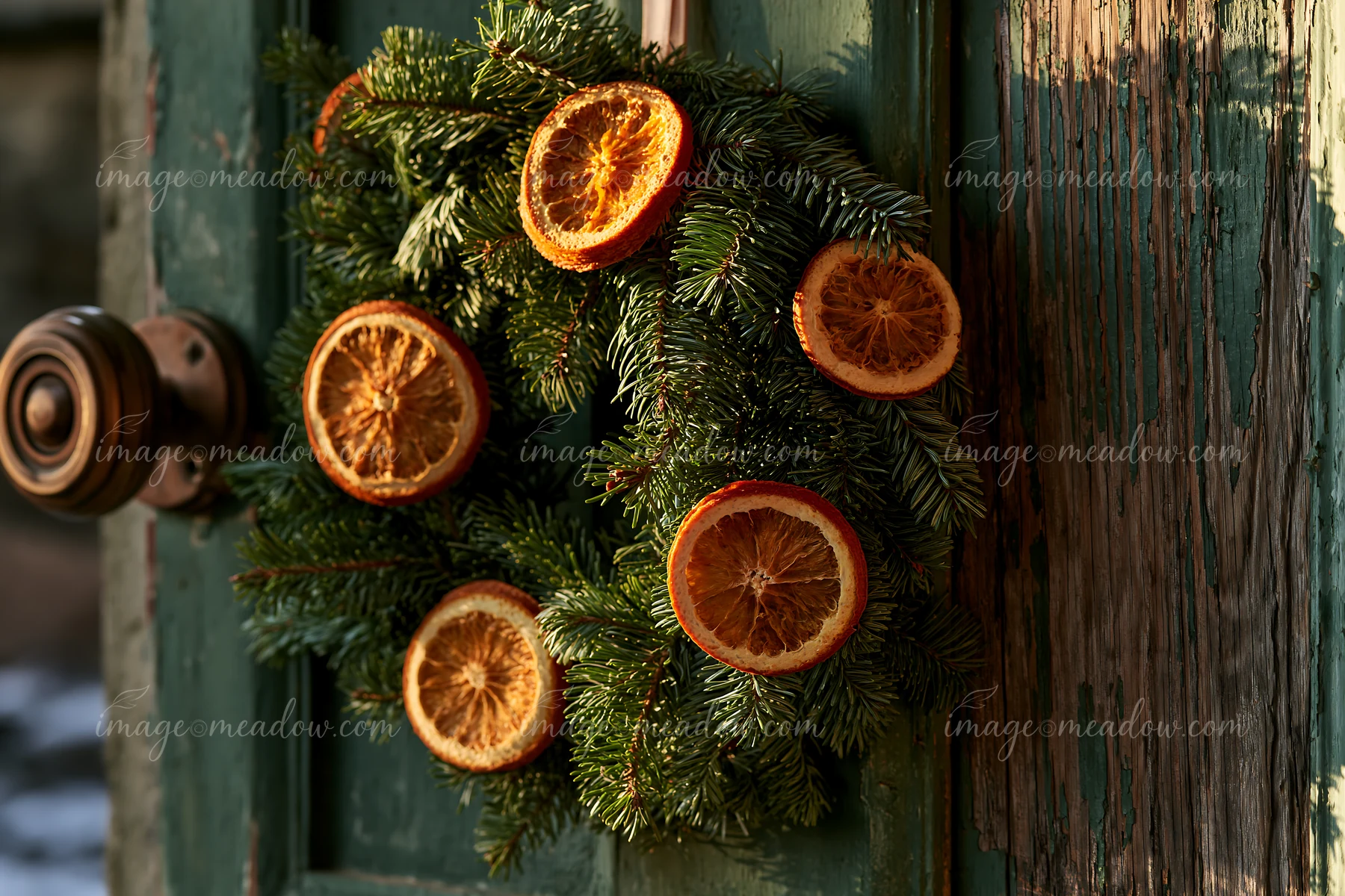 A Christmas wreath made of evergreen branches and dried orange slices hangs on a wooden apartment door, adding a festive touch to the entrance.